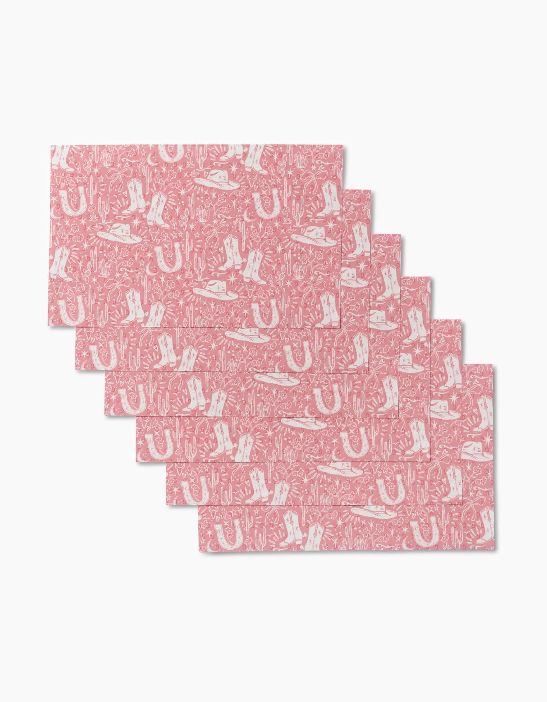 Six pink rectangular Cowgirl Chic placemats by Aubrey Fairchild, featuring white Western-themed patterns, are arranged in an overlapping formation on a white background. These reusable mats offer an eco-friendly alternative to Not Paper Towels.