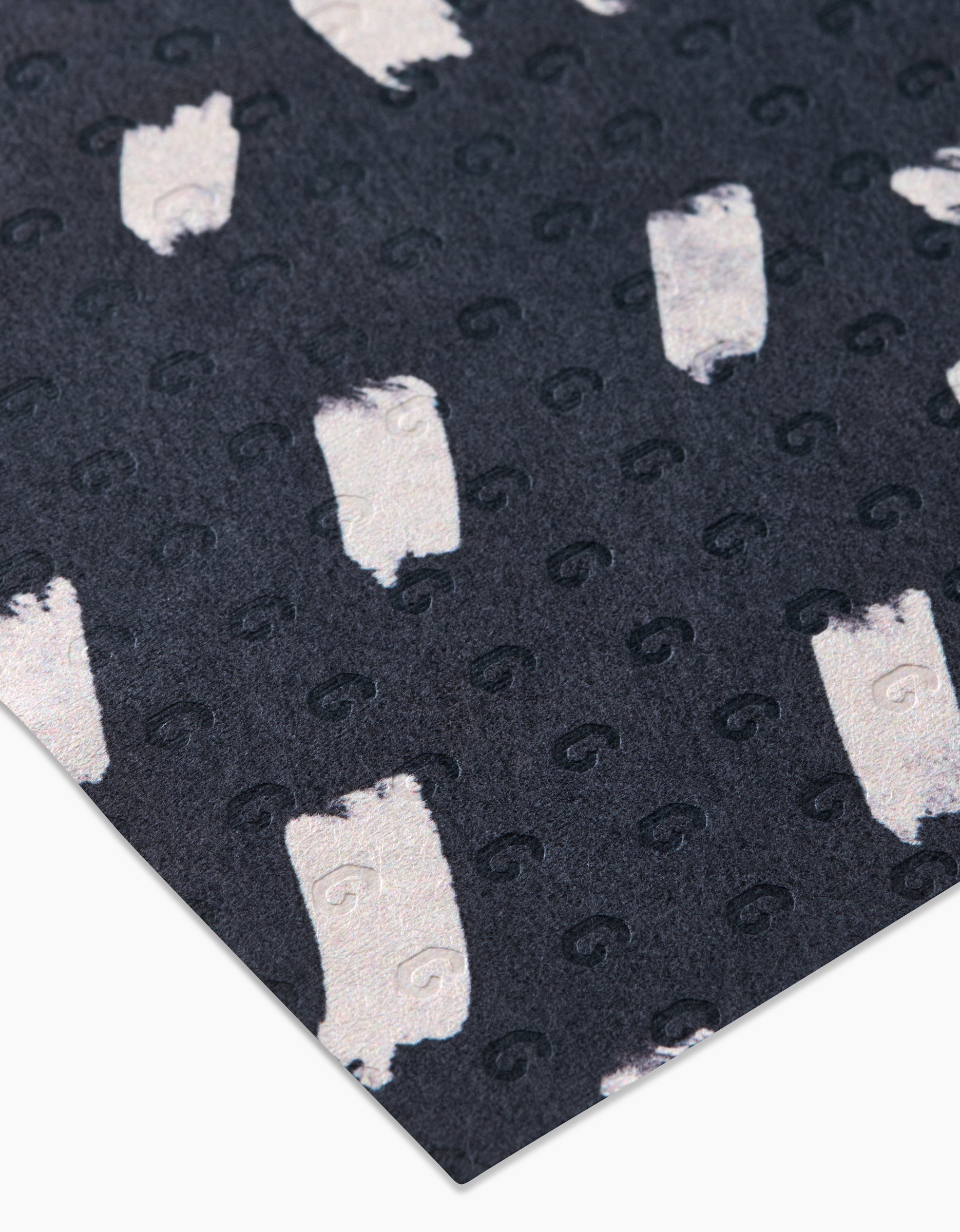 A close-up of GEOMETRY’s Dark Out surface, featuring small, shiny pale shapes and embossed swirls in a loose grid, made from post-consumer recycled materials.