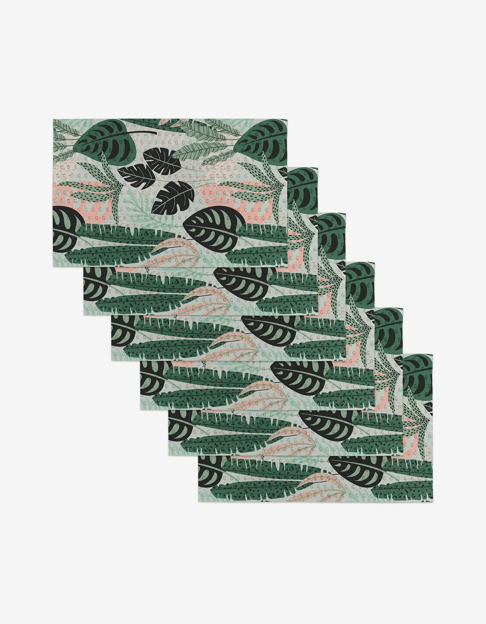 Six rectangular Diedre placemats by GEOMETRY, featuring a tropical leaf print in green, black, and light pink, are arranged in a step-like overlap on white—a reusable, eco-friendly alternative to paper towels.
