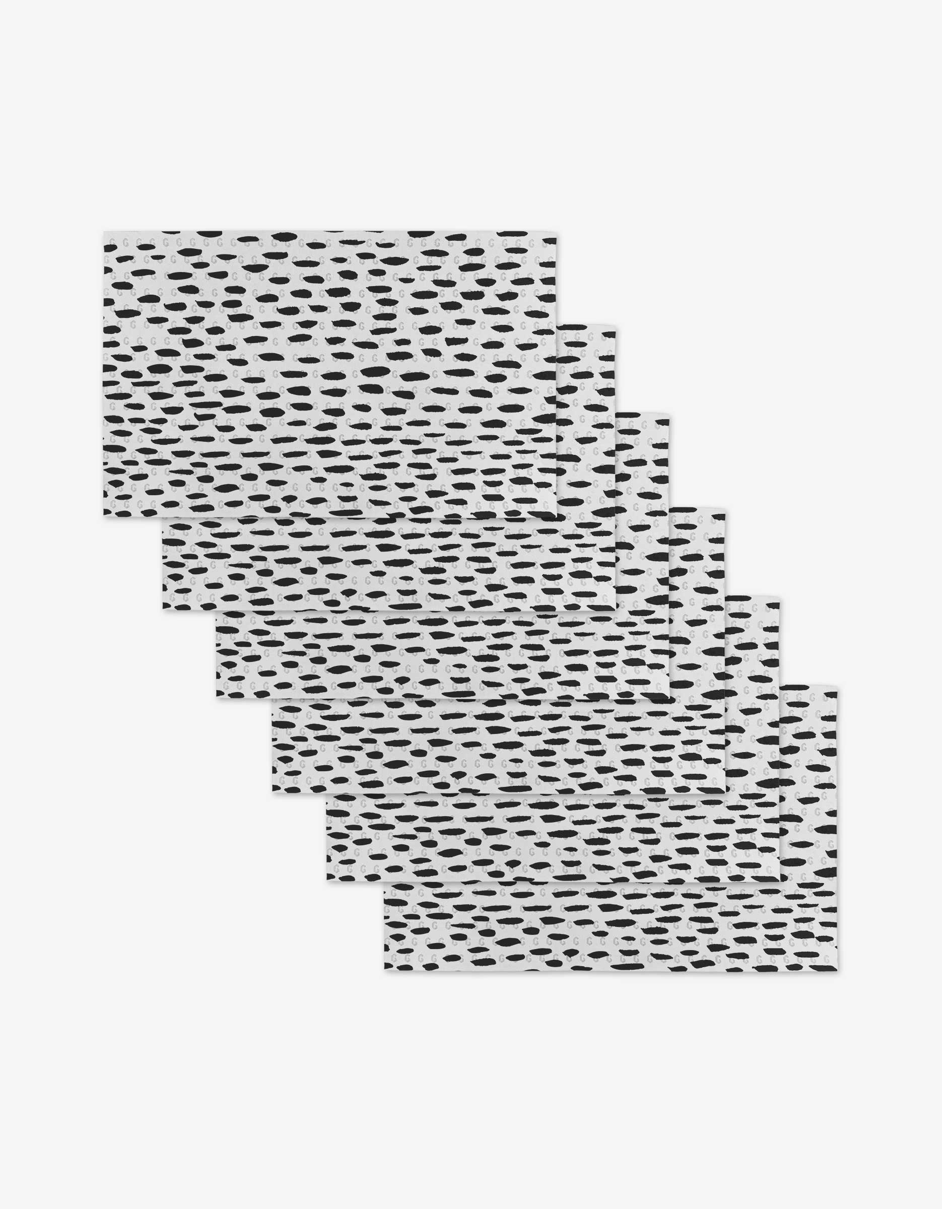 Six GEOMETRY Dot Dash rectangular placemats, featuring a white background with an irregular black dot pattern and made from post-consumer recycled materials, are arranged in a staggered stack on a plain white surface.