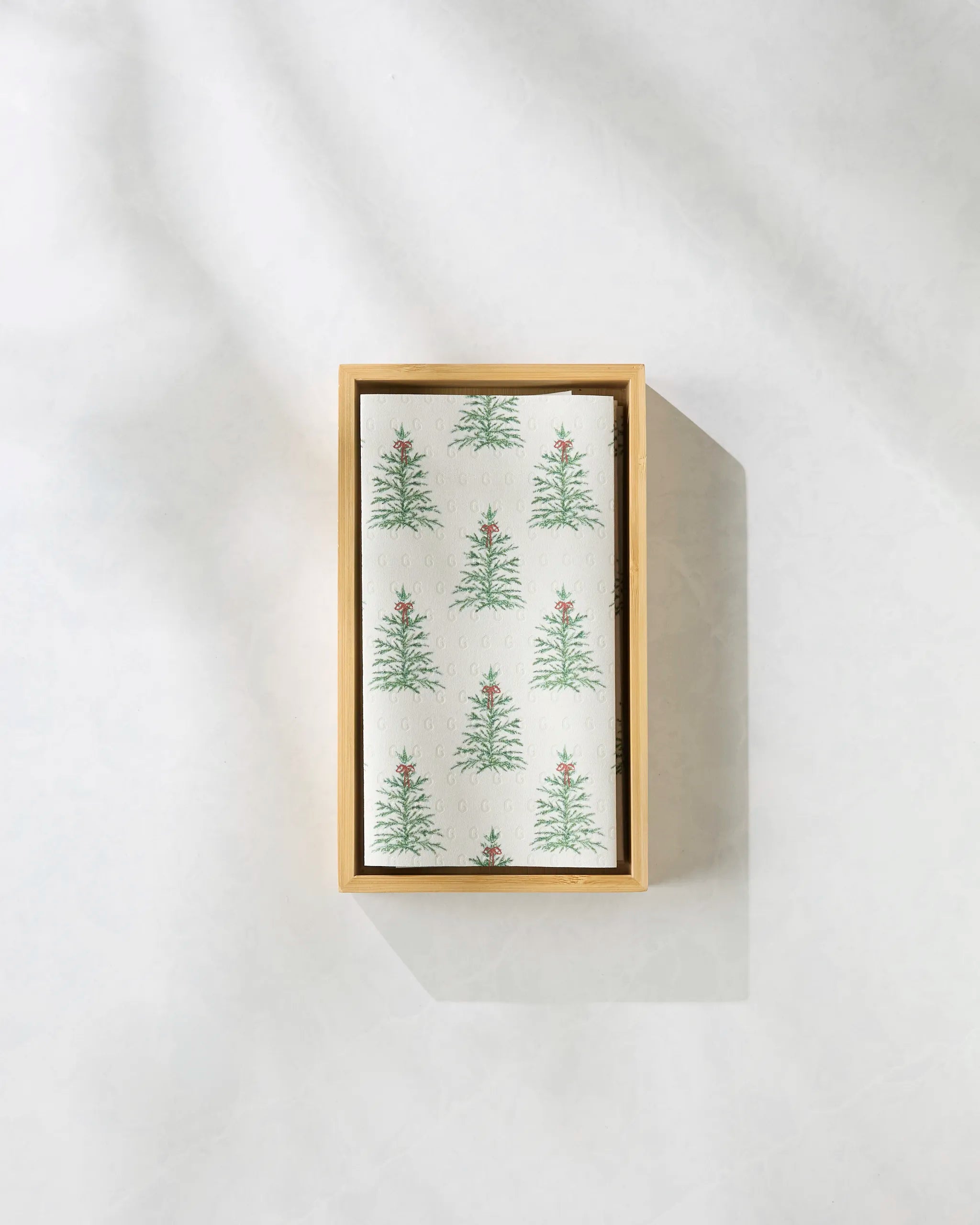 The Ellsworth by Geometry is a rectangular box featuring a card adorned with small Christmas trees topped with red stars on a light background—ideal for gifting eco-friendly paper towels. The box is displayed on a plain, textured surface.