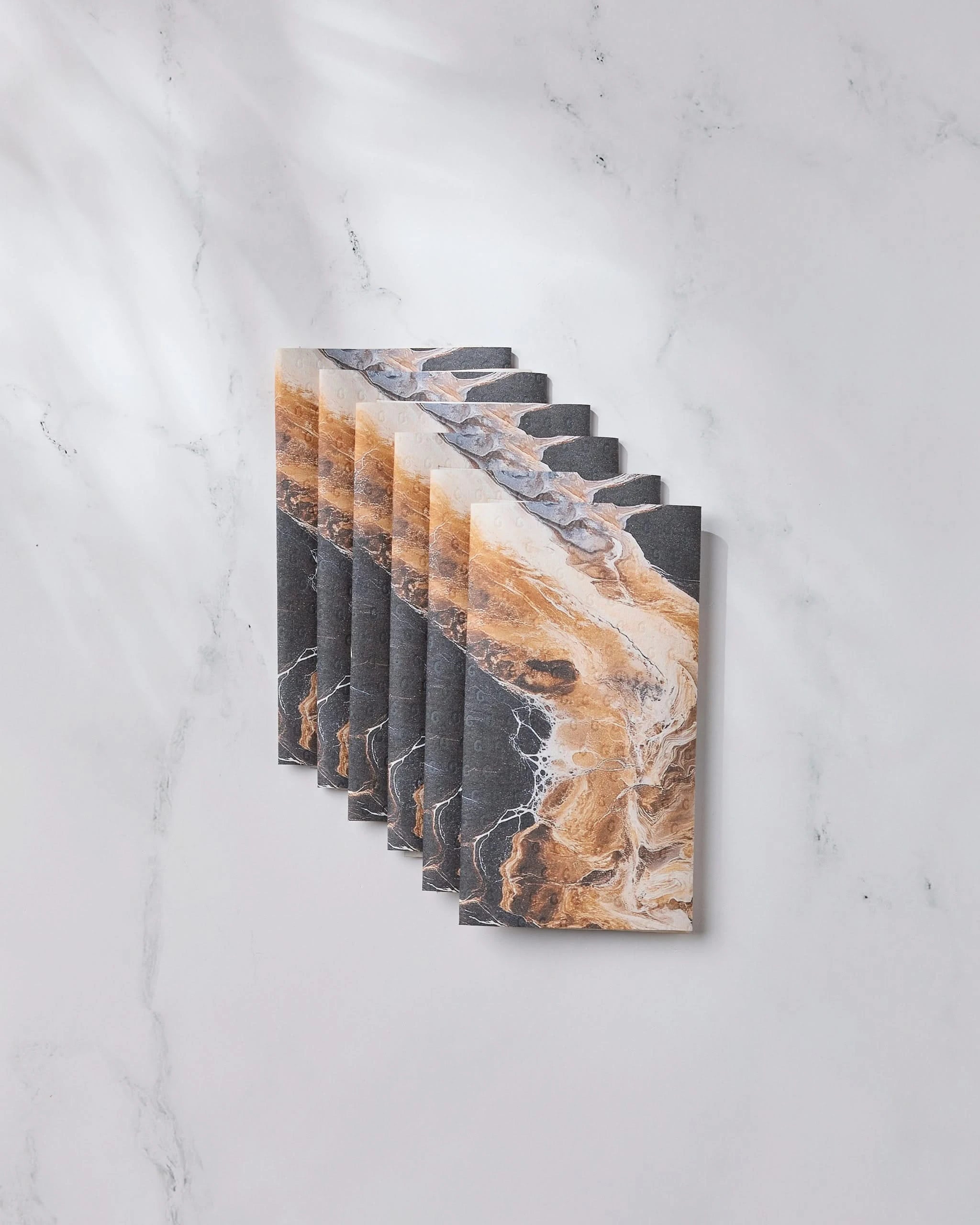 Geometry’s Emperador rectangular tiles in a black, tan, and white marbled pattern are artfully arranged in a staggered display on a white marble surface, with soft shadows and subtle light enhancing their eco-friendly appeal.