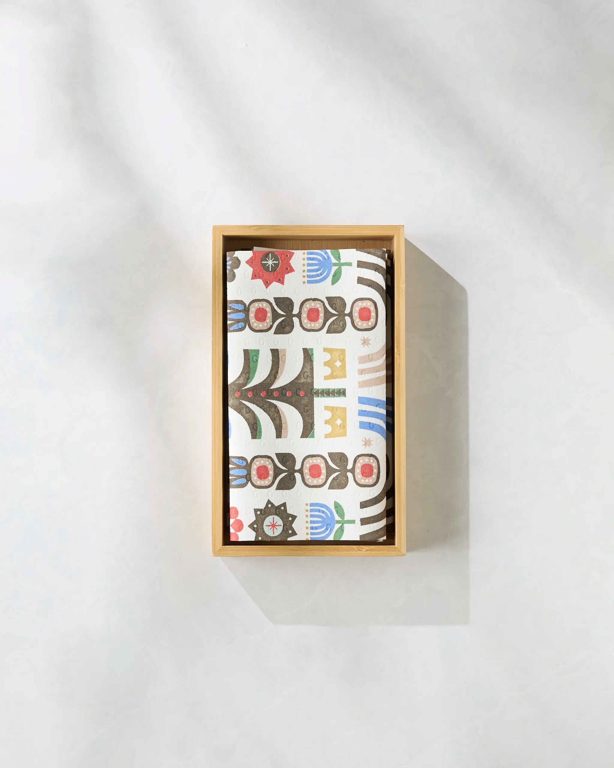 The Geometry Everfolk wooden box holds a stack of cards with a vibrant, abstract floral and geometric pattern, displayed on a light, textured surface.