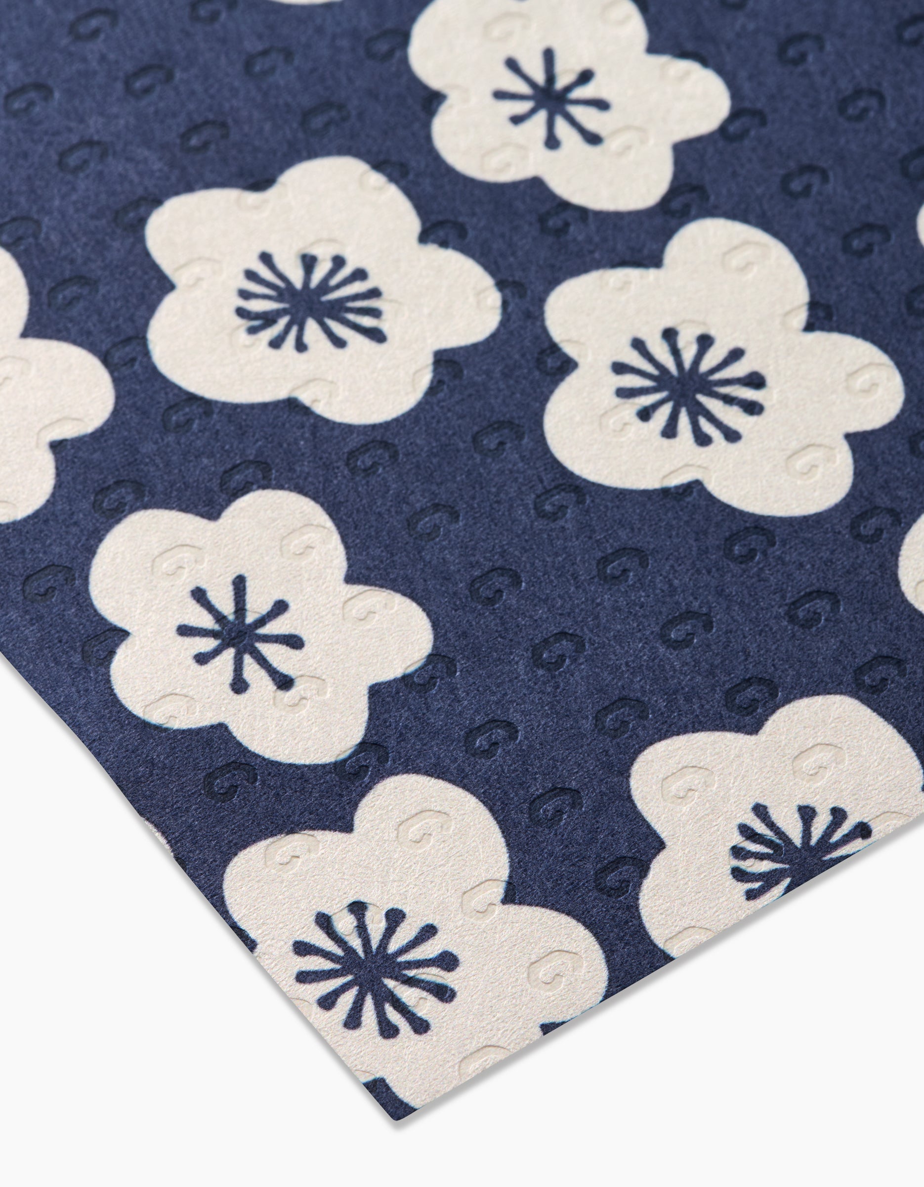 A close-up of GEOMETRYs Every Sunday shows blue textured fabric with repeating white five-petal flowers and dark blue centers. This eco-friendly option is ideal for reusable kitchen towels, displayed diagonally in the image.