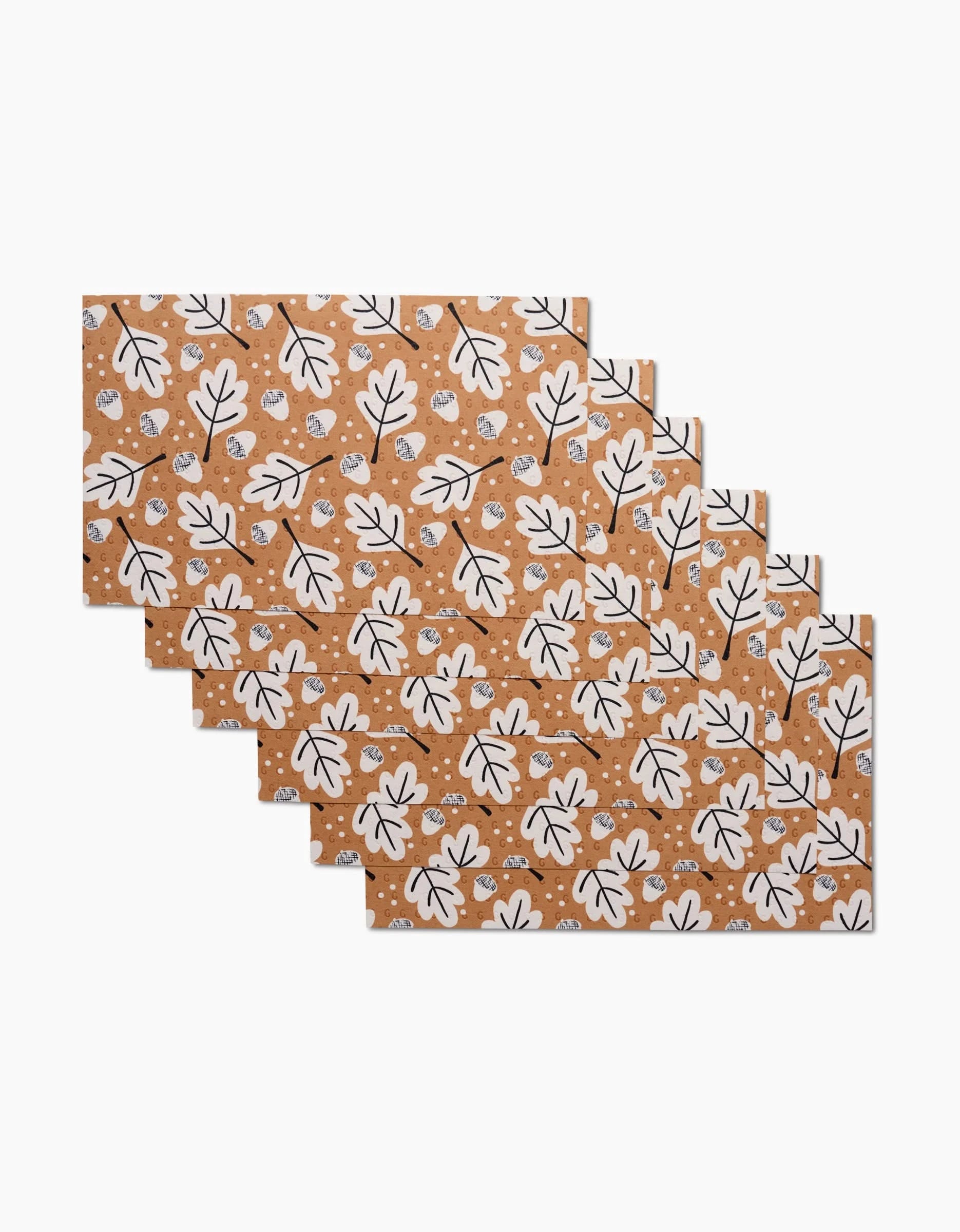 Six Falling Acorns placemats by Charlie Rowan Designs, featuring a brown background with white leaves and dots, fanned out—an eco-friendly alternative to traditional table settings.