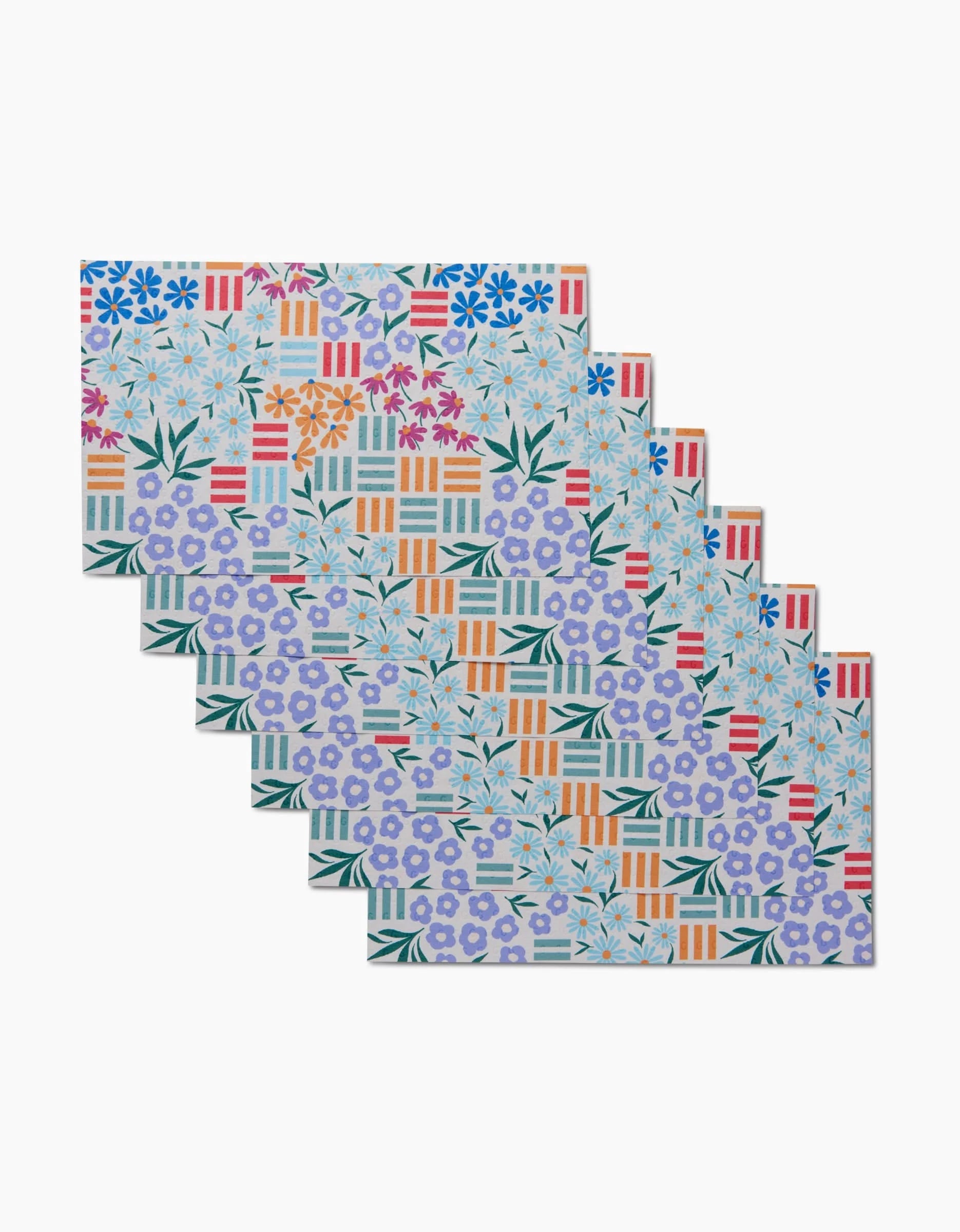 Floral Garden placemats by Charlie Rowan Designs include six colorful, rectangular mats made from post-consumer recycled materials, featuring vibrant repeating floral and geometric patterns in blue, violet, orange, green, and red.