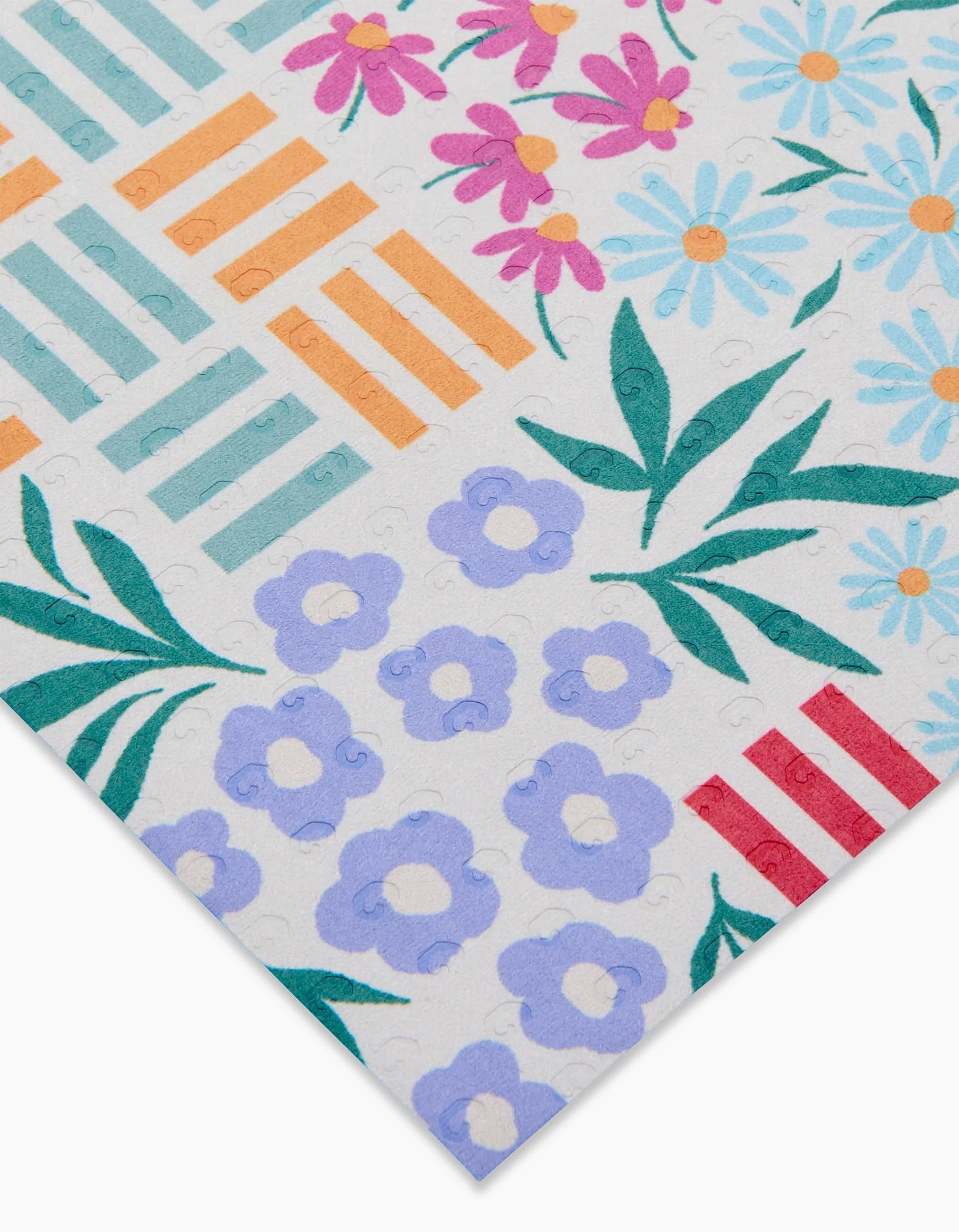 Floral Garden by Charlie Rowan Designs features a vibrant white background with orange and red rectangles, purple flowers, blue daisies with yellow centers, green leaves, and pink flowers—crafted from eco-friendly recycled materials.