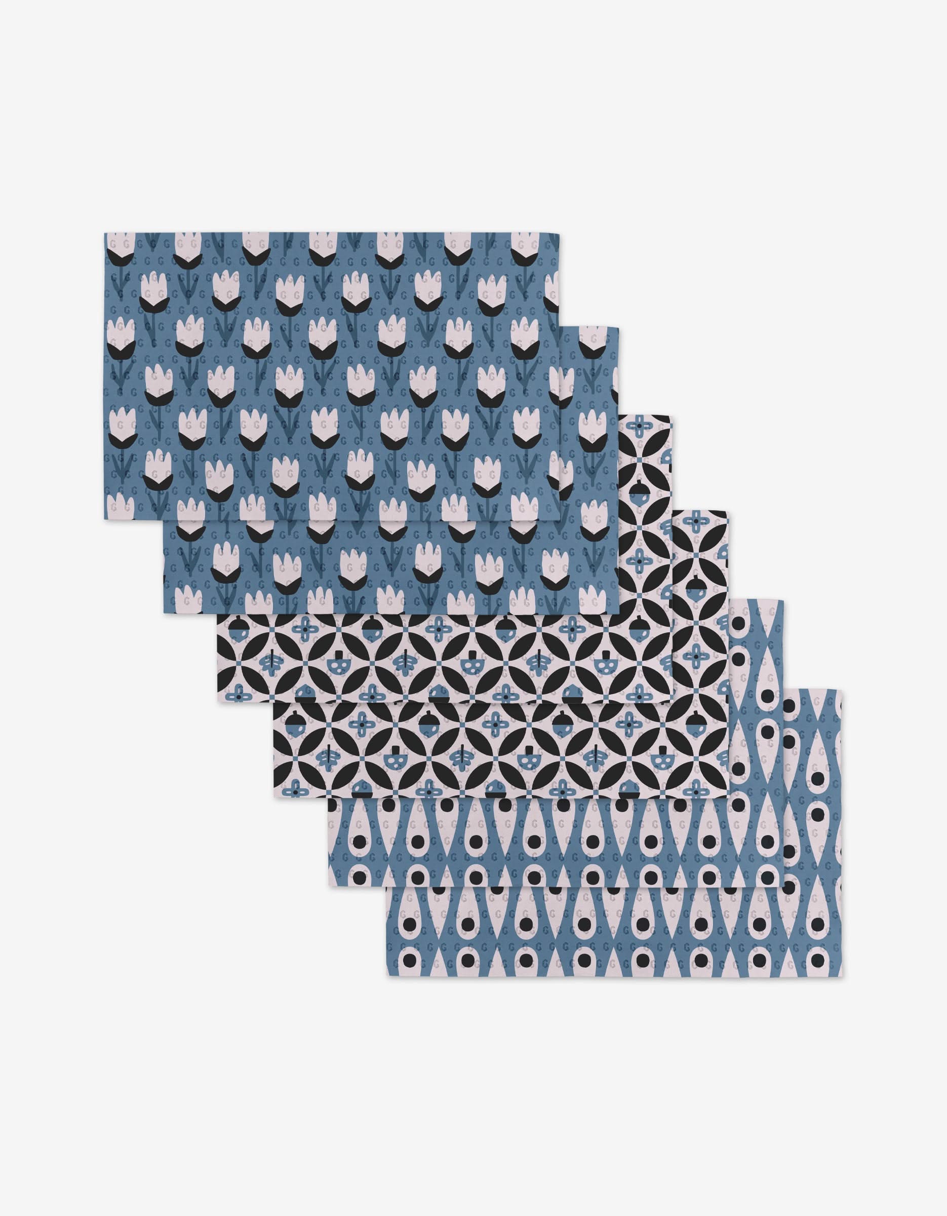 Five Forest Findings rectangular placemats by Anette Heiberg, featuring blue, black, and white geometric and floral patterns, are stacked on a white background—an eco-friendly alternative to paper towels.