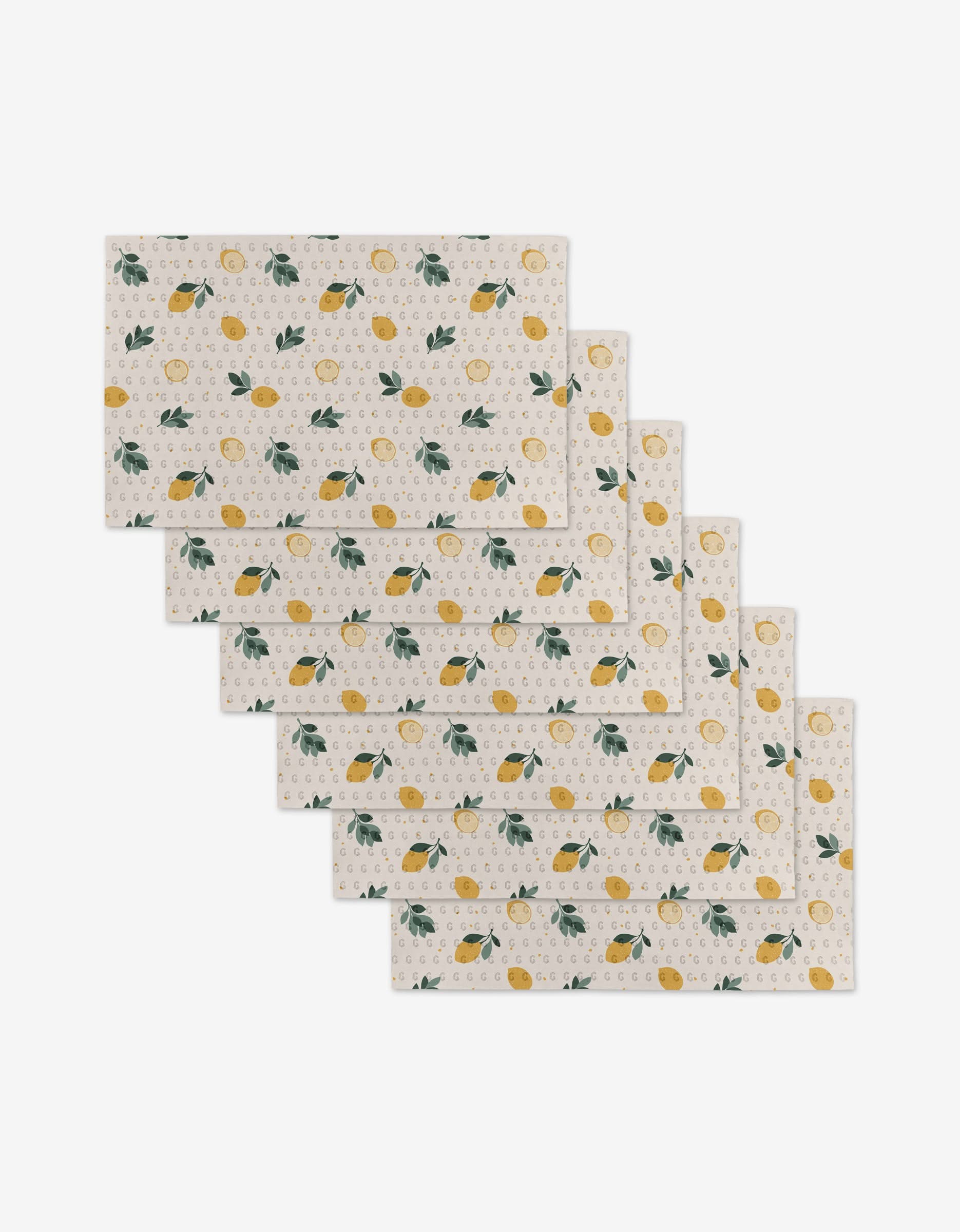 Seven Freshly Picked rectangular placemats by Sara Mari, featuring a white background with yellow lemons, green leaves, and beige dots. Made from eco-friendly materials and stacked with slight overlap; not paper towels.
