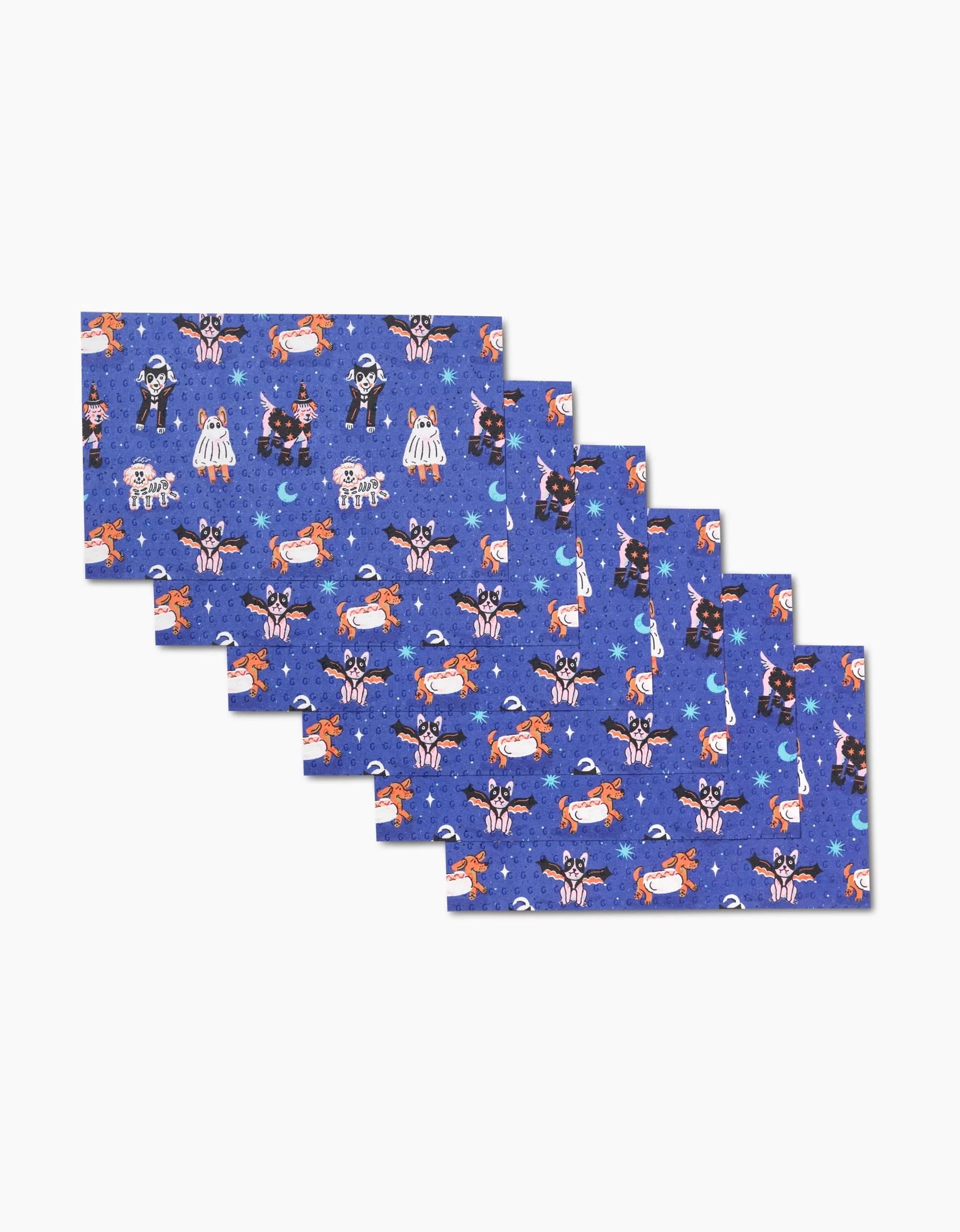 Six Halloween Hounds reusable napkins by Camila Leão, with a blue background and a festive pattern of skeletons, black cats, pumpkins, ghosts, bats, and moons. The rectangular napkins are neatly stacked and slightly overlapped.