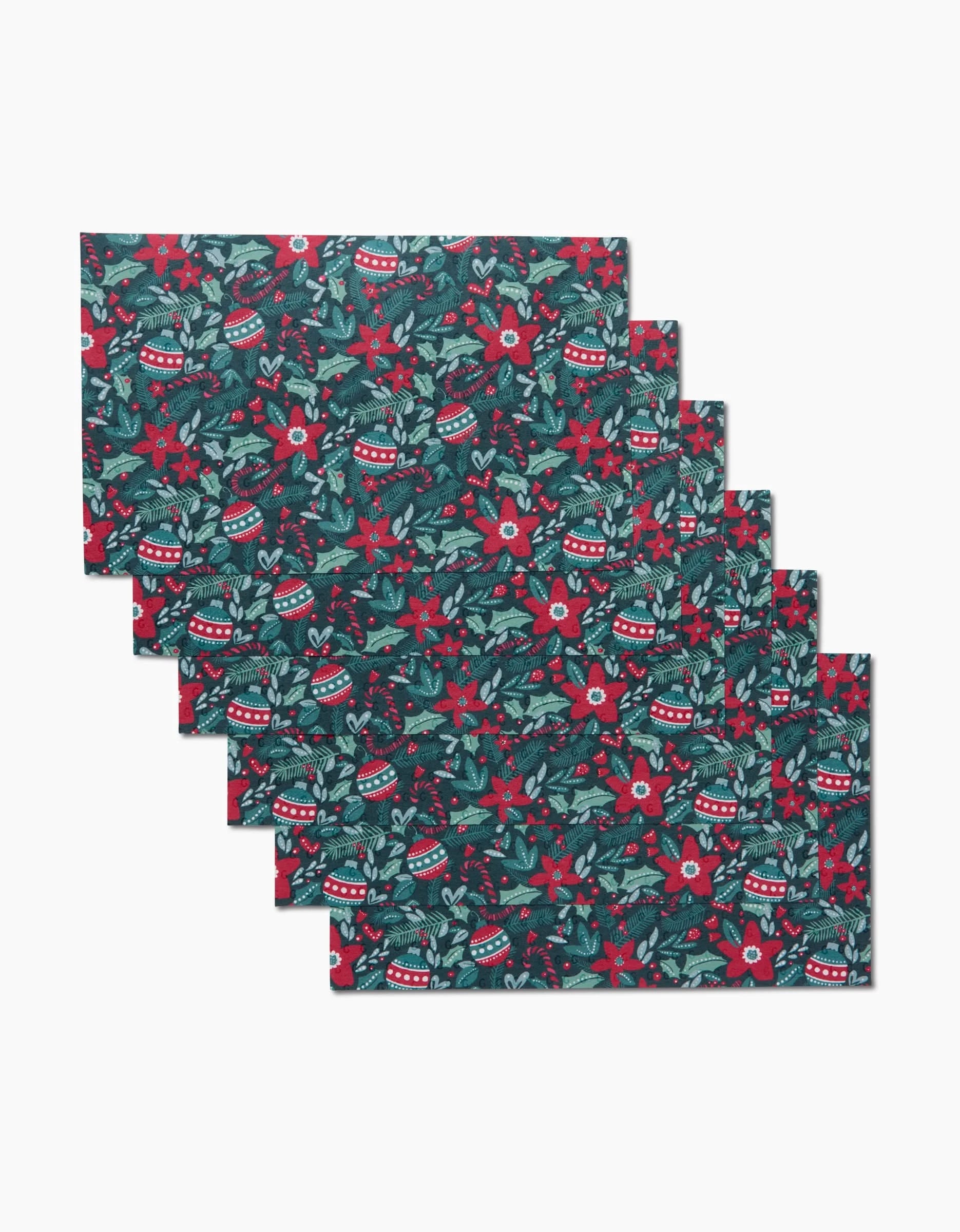 The Kris Ruff Happy Christmas set includes six rectangular placemats with red poinsettias, green leaves, and ornaments on a dark background—an eco-friendly, machine-washable alternative to disposable decor.