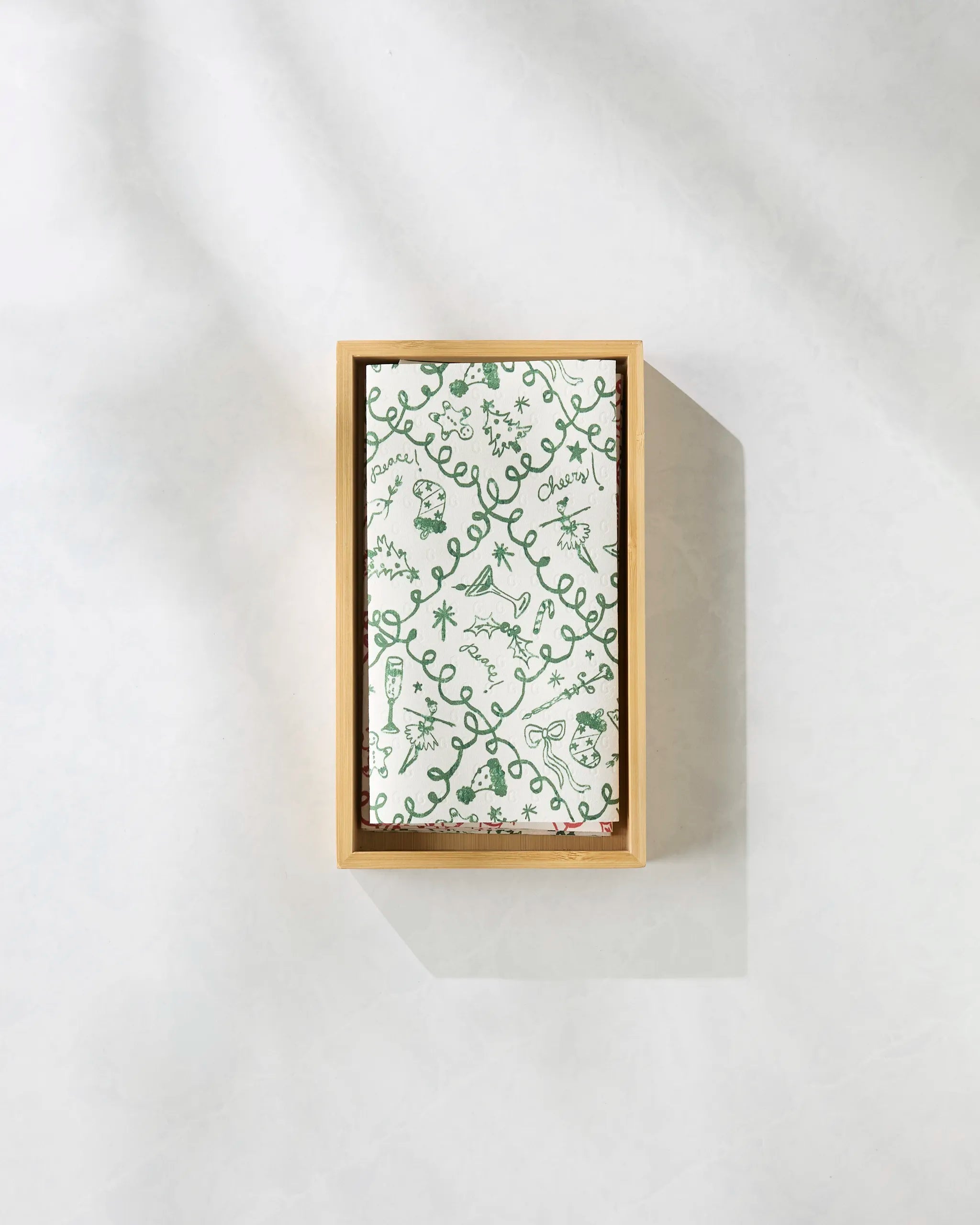 Geometry’s Holiday Doodling features an eco-friendly paper towel with whimsical green line plant and animal doodles on a softly shaded white background, displayed in a rectangular wooden tray.