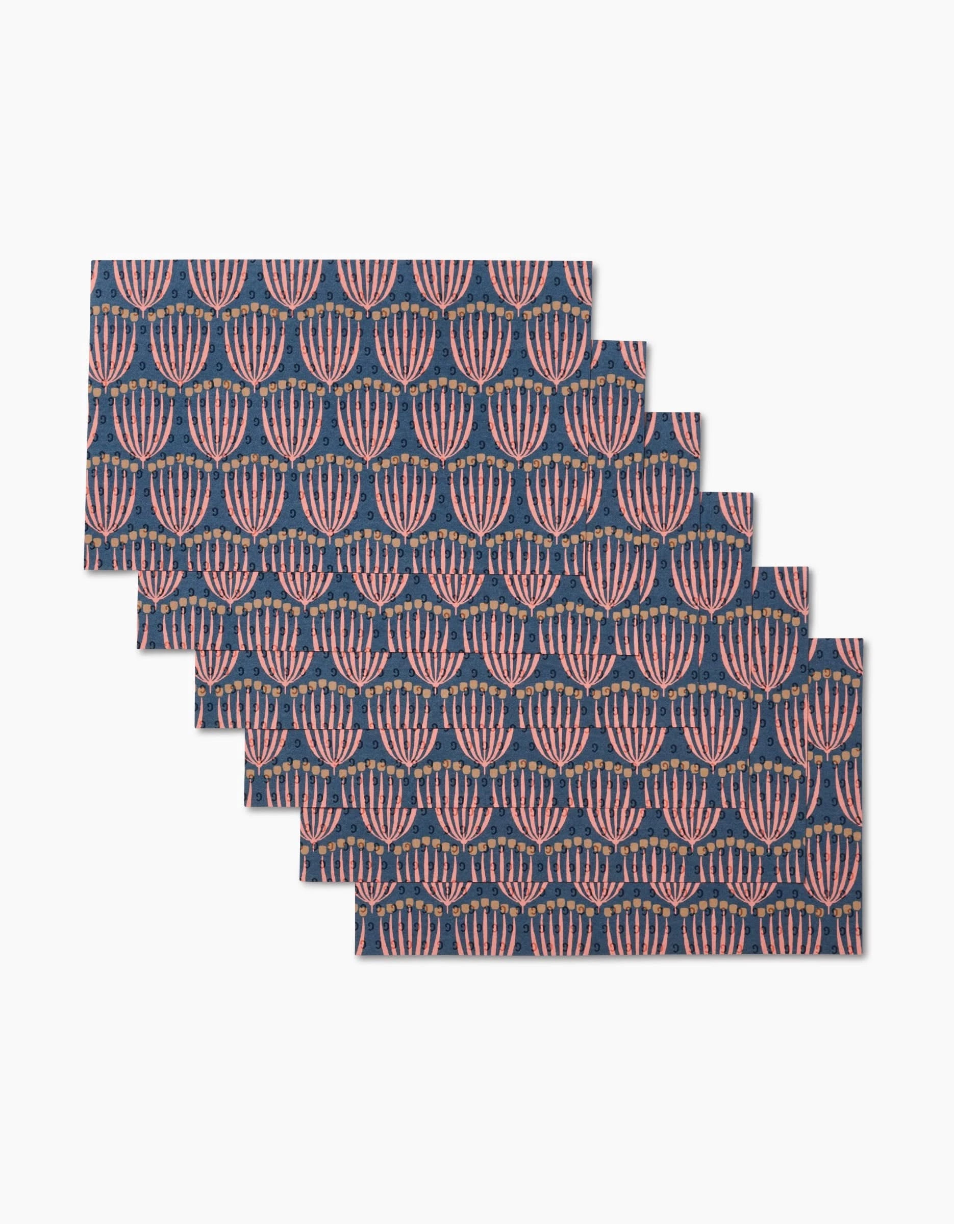 Six Josie rectangular placemats by Amy MacCready are stacked in a staggered arrangement, each showcasing pink and red abstract floral patterns on dark blue—an eco-friendly design made with post-consumer recycled materials.