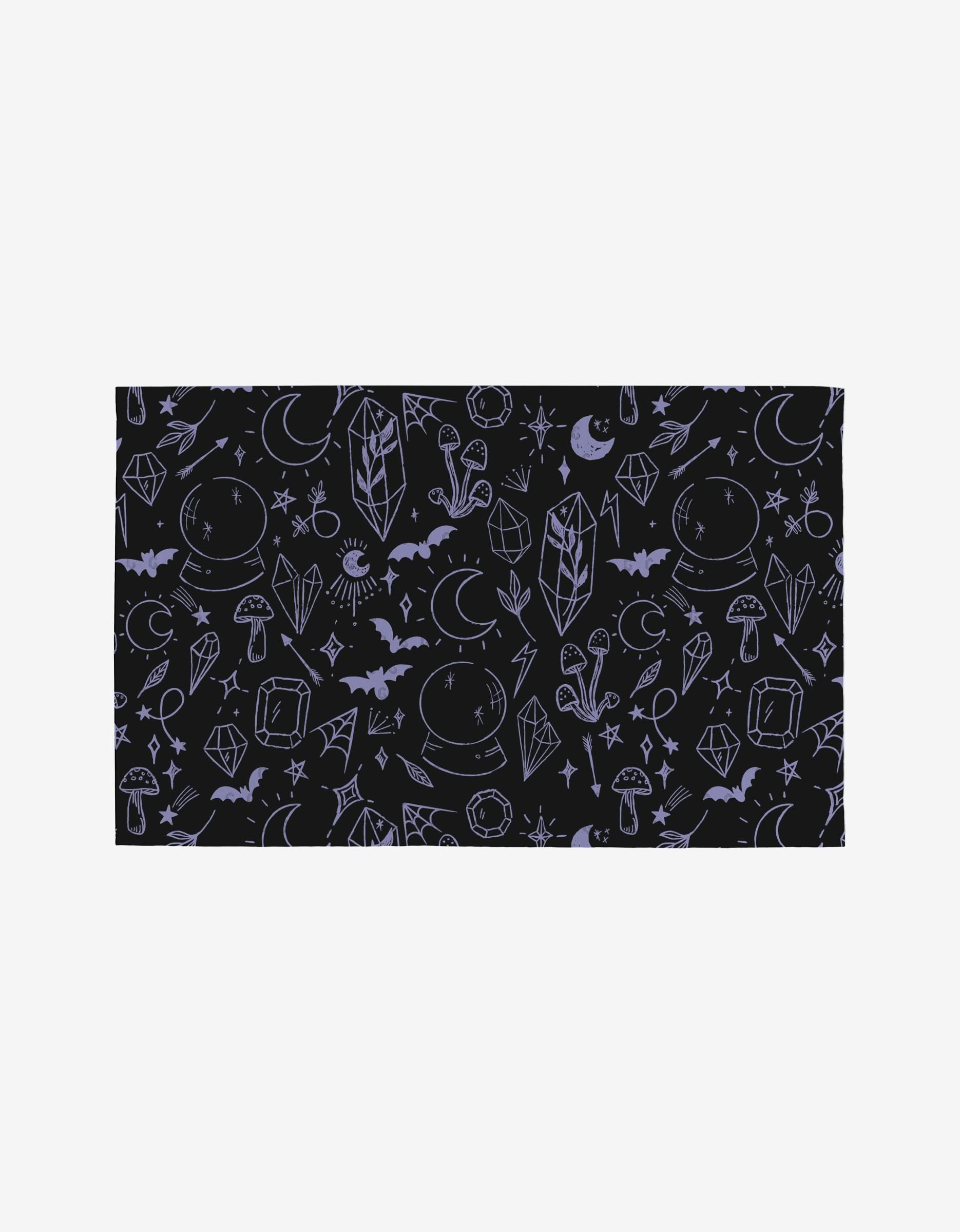 Magic Spells by Hufton Studio: a black rectangular cloth featuring purple mystical symbols—crystals, bats, moons, stars, mushrooms, and magic balls—crafted from eco-friendly post-consumer recycled materials.
