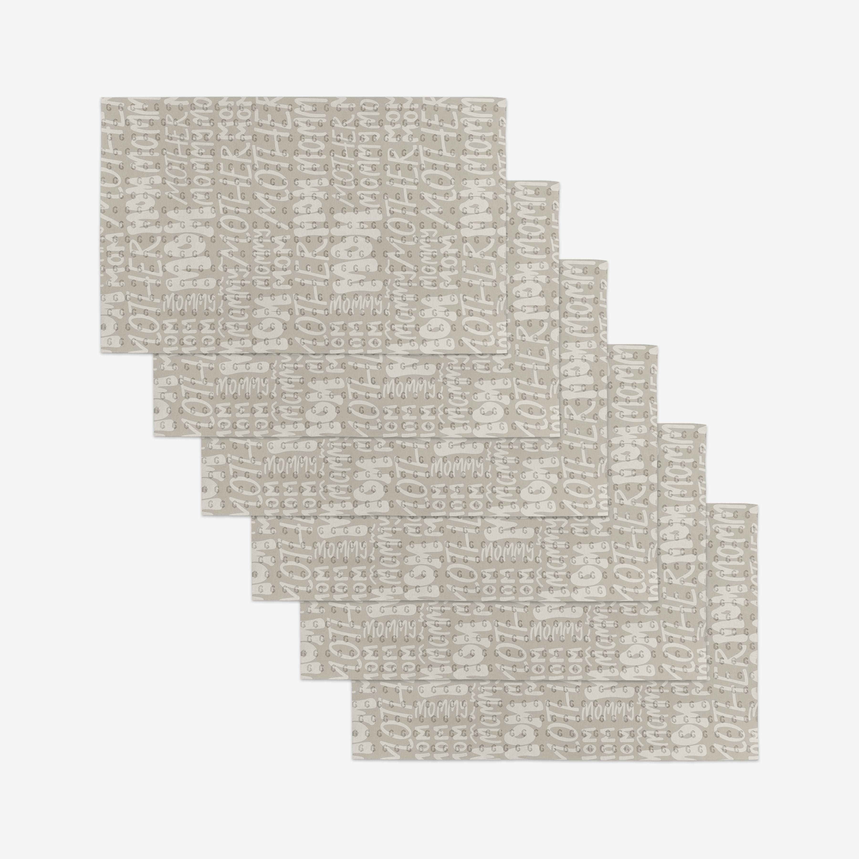 Seven beige rectangular GEOMETRY Mom placemats featuring a white abstract pattern, made from eco-friendly materials, are arranged in a staggered, overlapping layout on a white background.