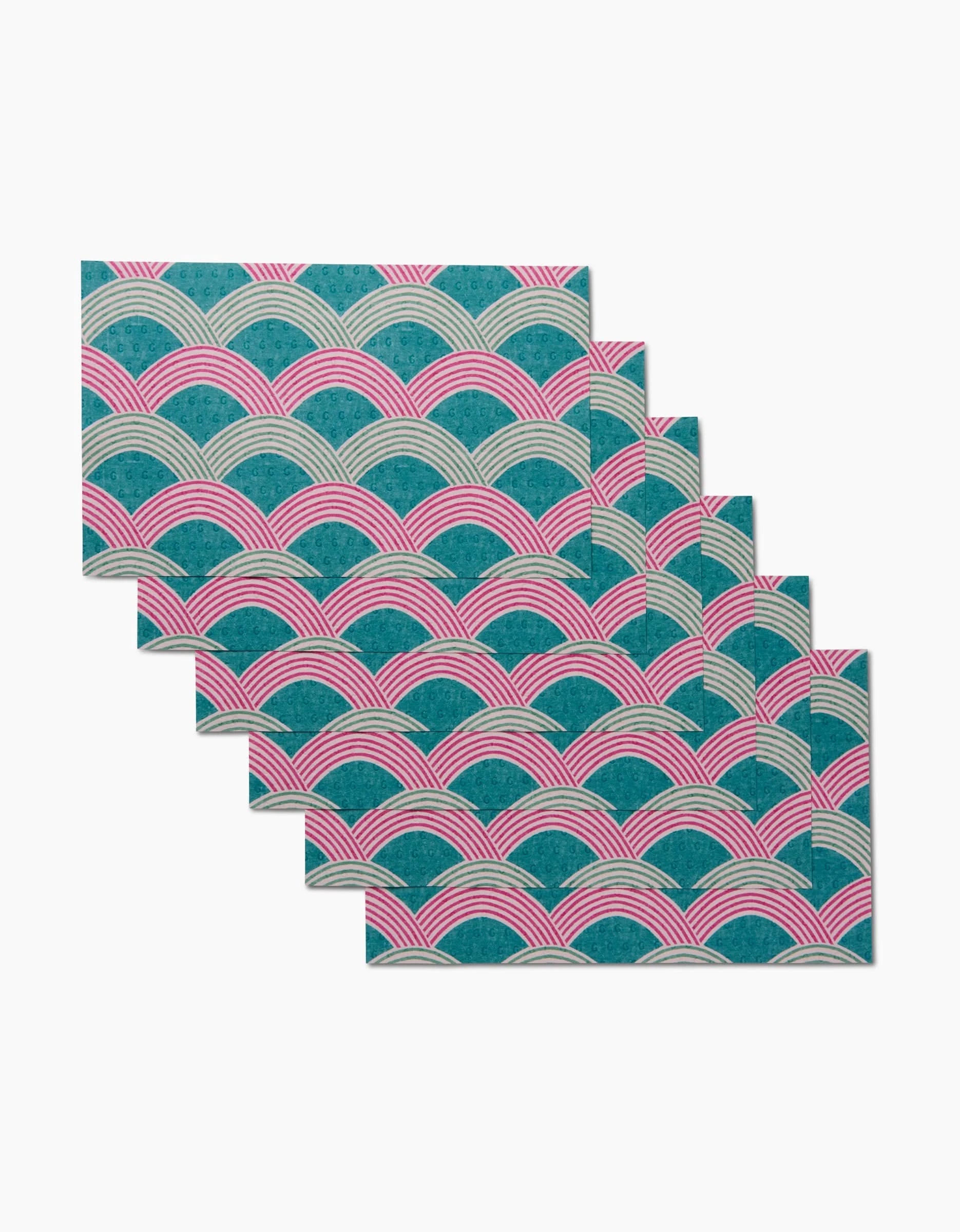 Six Nalin rectangular placemats by Amy MacCready, featuring a repeating scallop pattern in teal, pink, and white and made from eco-friendly recycled materials, are arranged in a staggered stack on a white background.