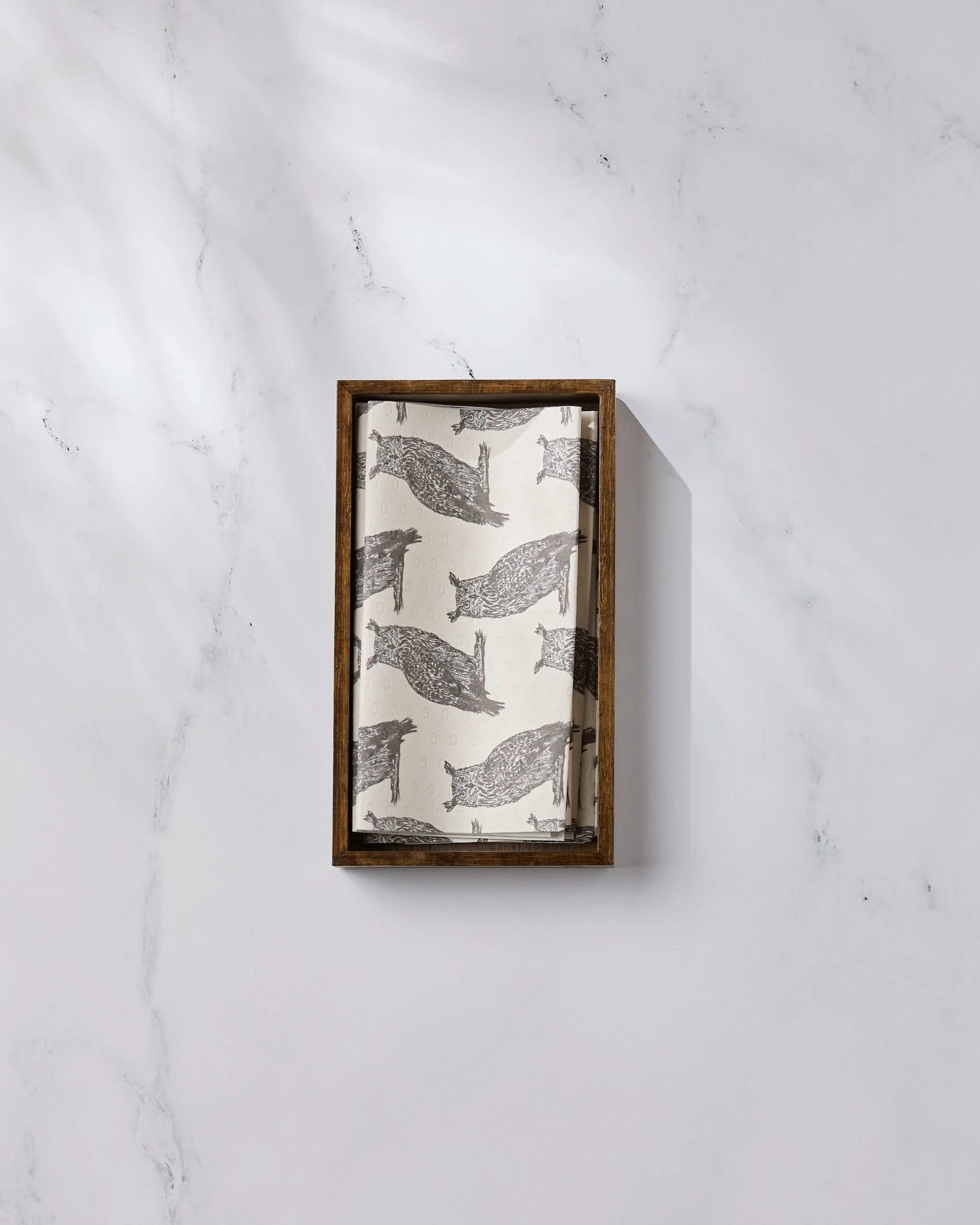 A rectangular wooden tray holds Nocturne, an eco-friendly kitchen towel by Geometry with a repeating black narwhal print, ideal for replacing paper towels—all displayed on a white marble surface.