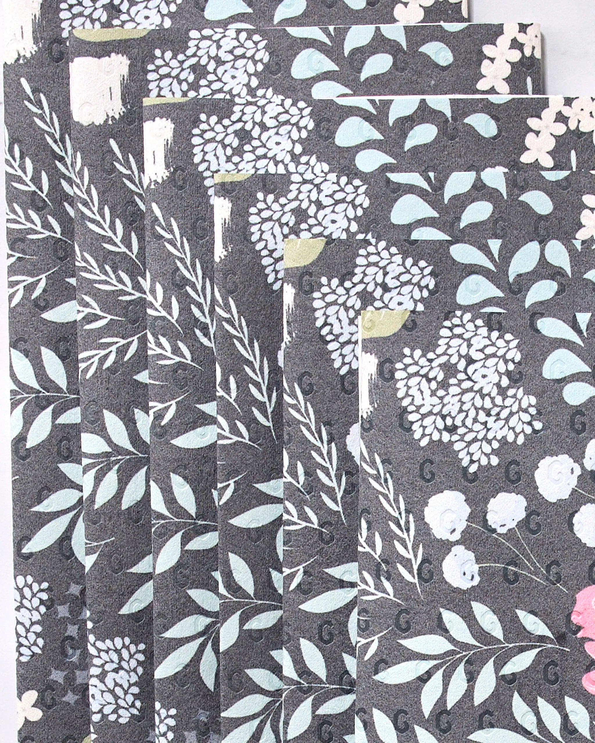 Not Forgotten by GEOMETRY features several dark, reusable paper towels with a repeating floral pattern in light blue, teal, white, pink, and yellow arranged in a fanned-out display.