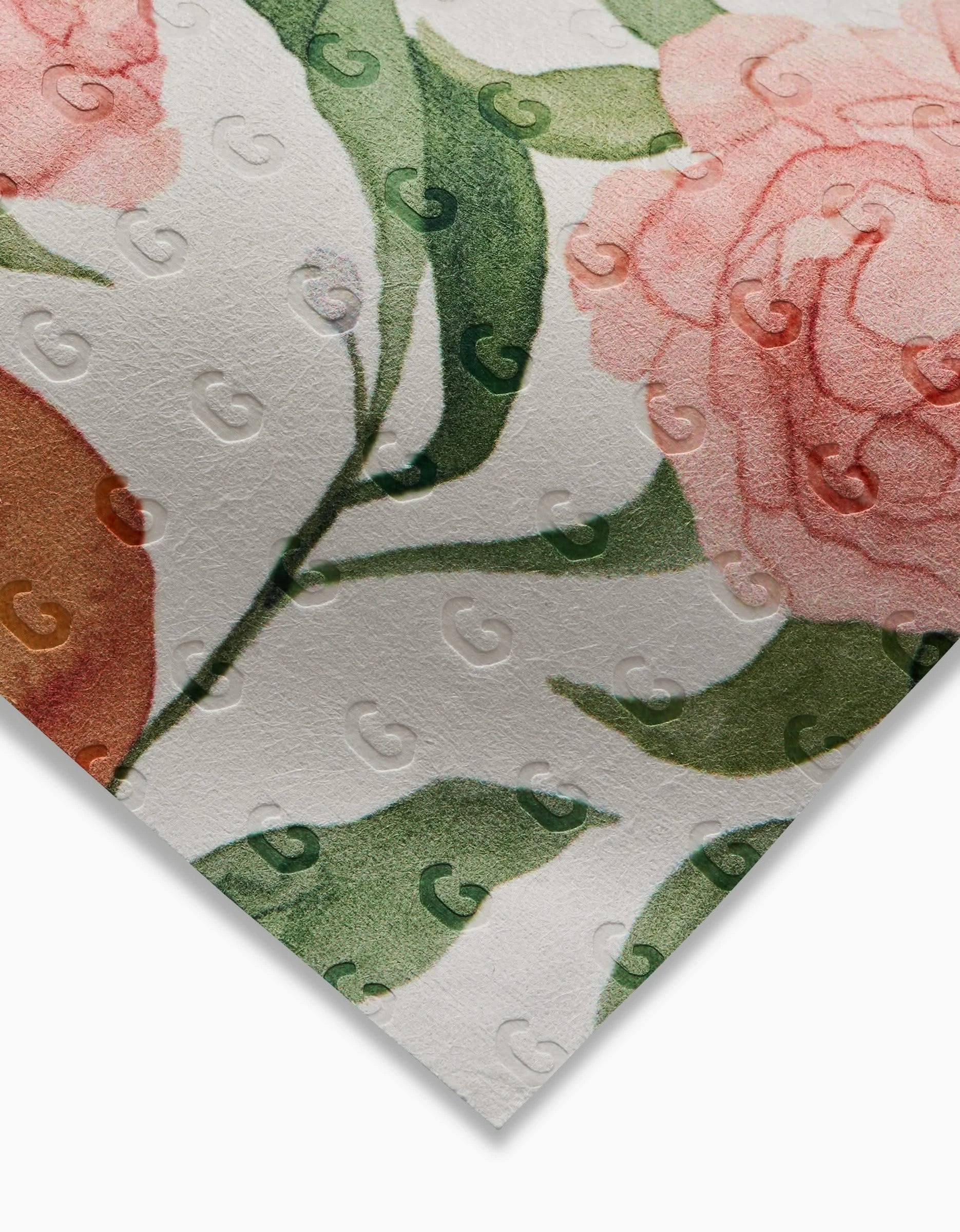 A close-up of Aubrey Fairchild’s “Peony For Your Thoughts” floral-patterned paper, made from eco-friendly post-consumer recycled material, with pink and peach flowers, green leaves, and a subtle embossed G logo visible at an angle.