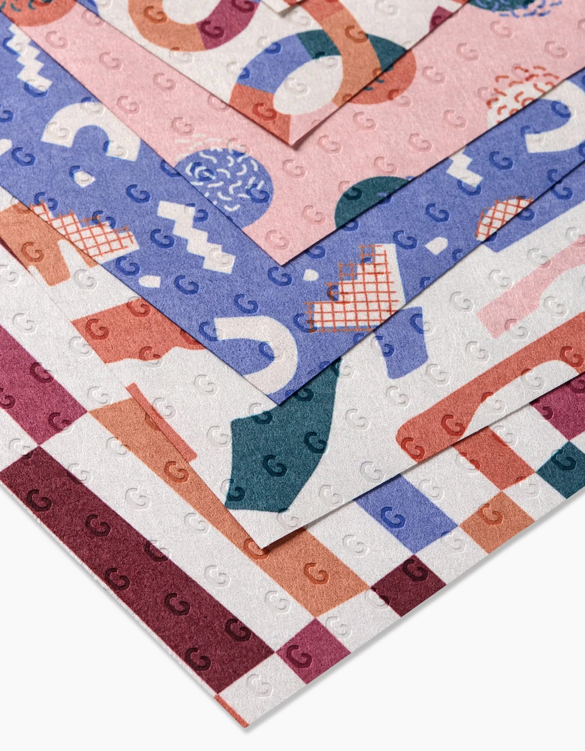 Rainbow Cutouts by Claire Iglesias: four stacked sheets of patterned, post-consumer recycled paper with colorful abstract shapes—squiggles, checks, and geometric designs—in pink, blue, maroon, and orange.