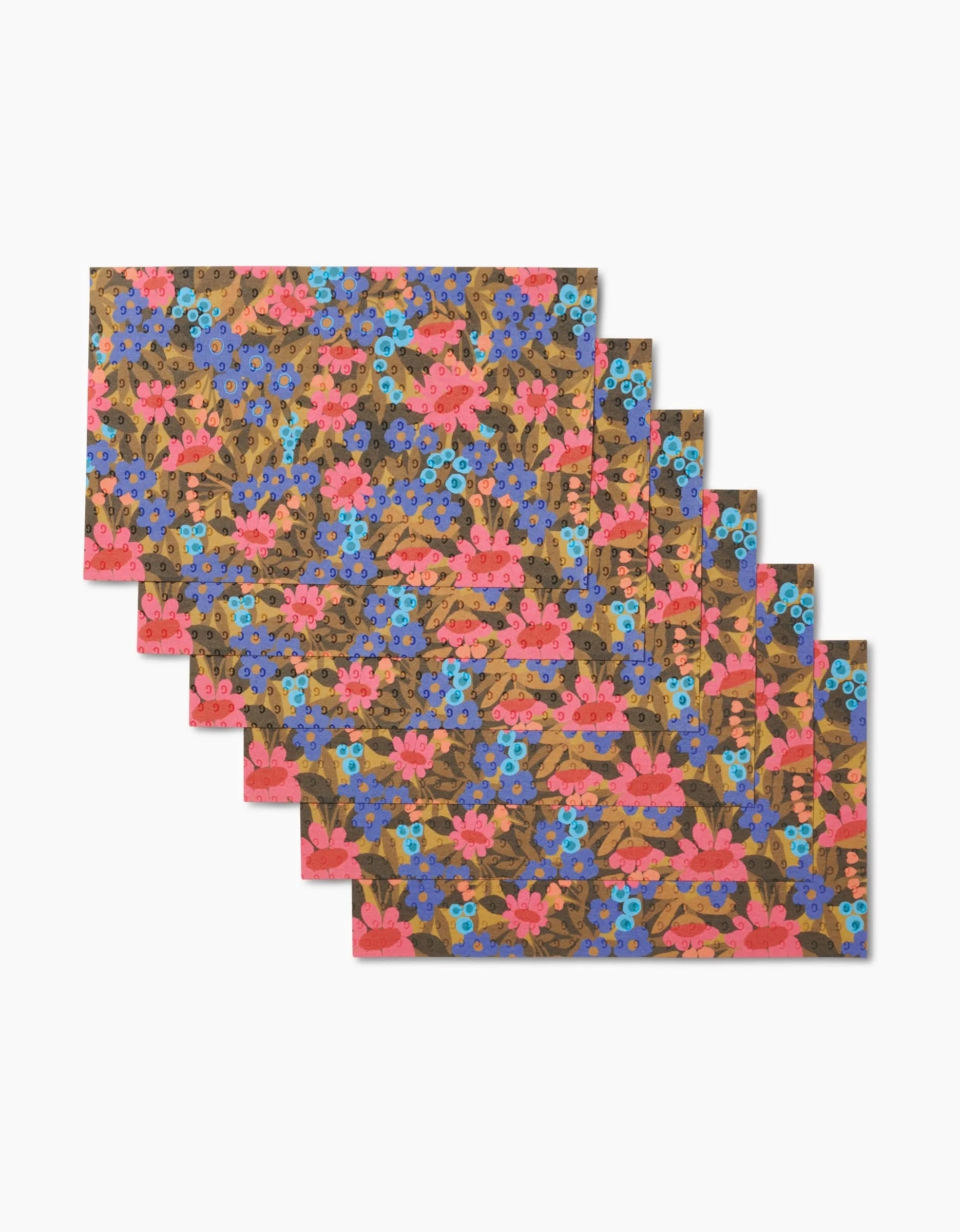 Six rectangular Retro Garden placemats by Lisa Nelson, featuring a colorful floral pattern in pink, blue, orange, and green on recycled materials, are stacked on a white background.