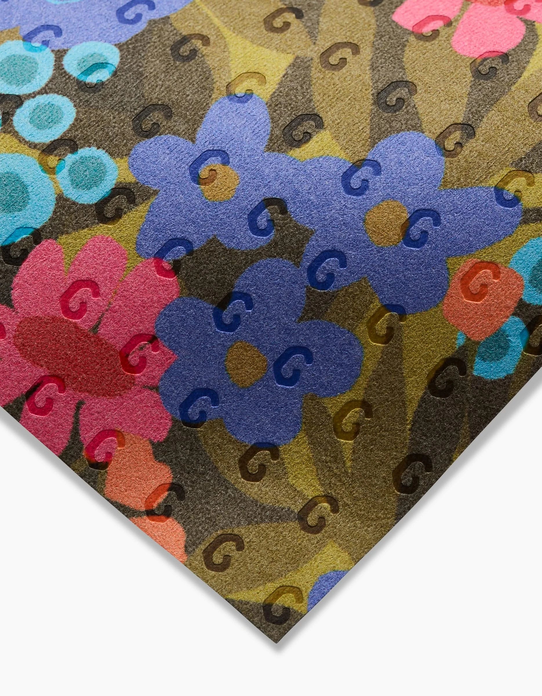 A close-up of Retro Garden fabric by Lisa Nelson shows blue and pink flowers with circular designs, green leaves, and turquoise accents on brown. This Not Paper Towels fabric is made from recycled materials and rests on a white surface.