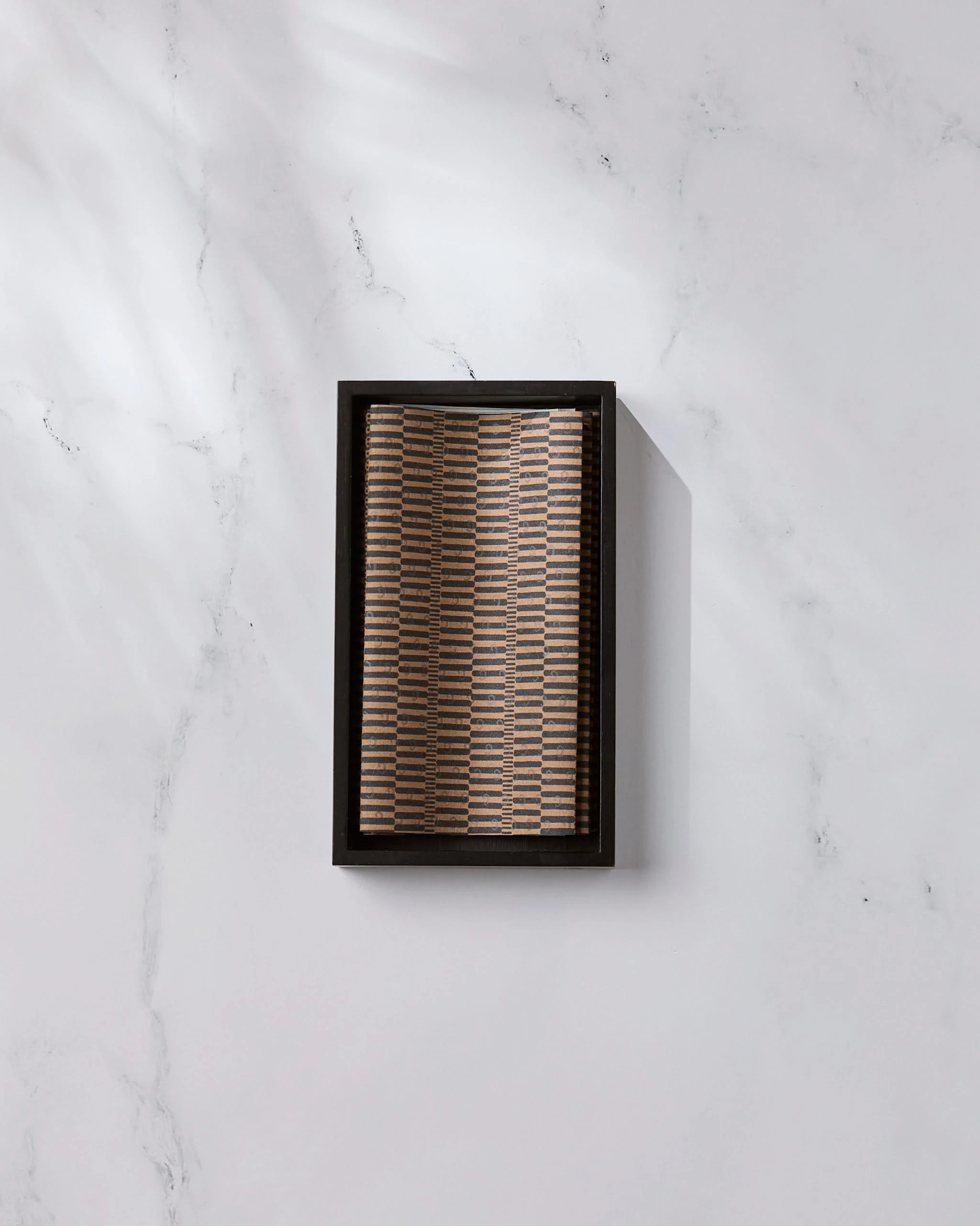 A rectangular box of Ridge eco-friendly kitchen towels by Geometry, featuring a woven patterned lid, rests on white marble with light reflections and subtle veining casting a soft shadow to the right.