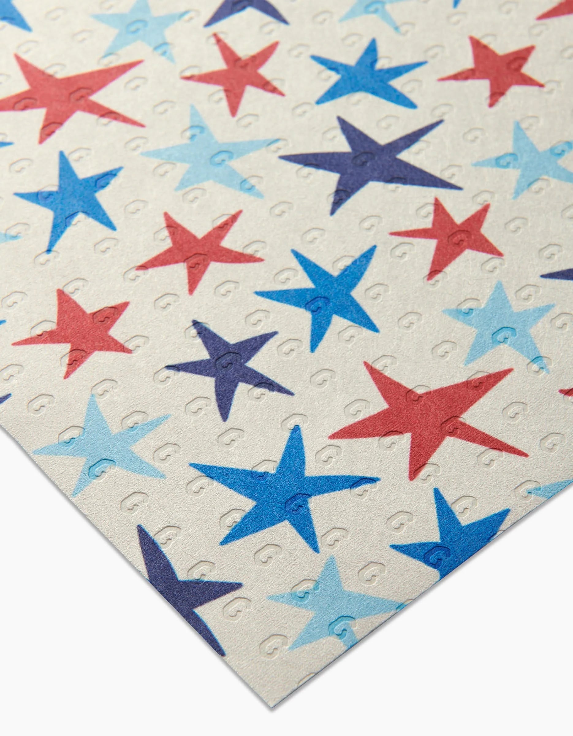 The Seeing Stars sheet by Mindfulnice is made from post-consumer recycled paper, featuring a cream background with red, light blue, and dark blue stars in a repeating pattern and small embossed Gs between the stars.