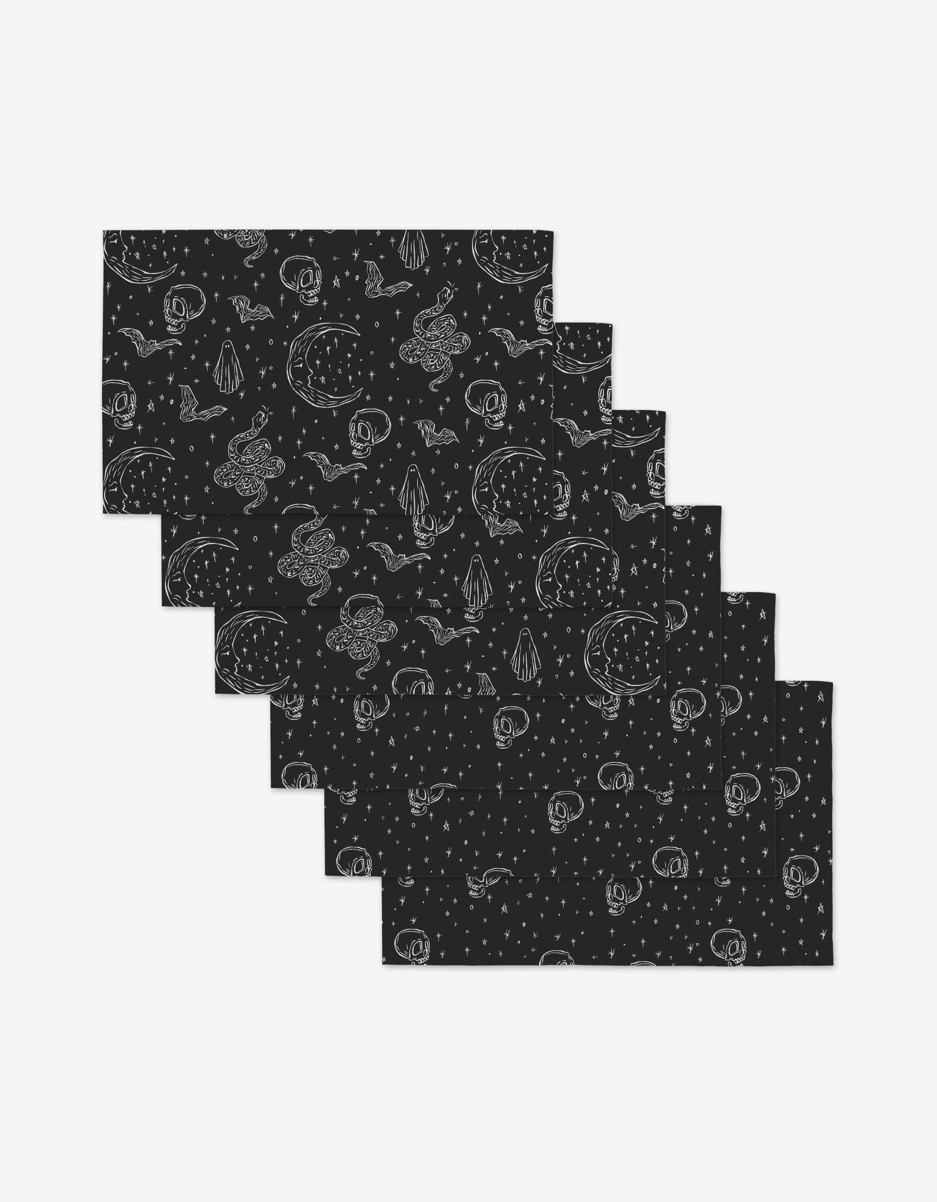 Six black rectangular Skulls and Stars placemats by Aubrey Fairchild, featuring white hand-drawn space-inspired designs, are arranged in a staggered overlap—eco-friendly and made from post-consumer recycled materials.