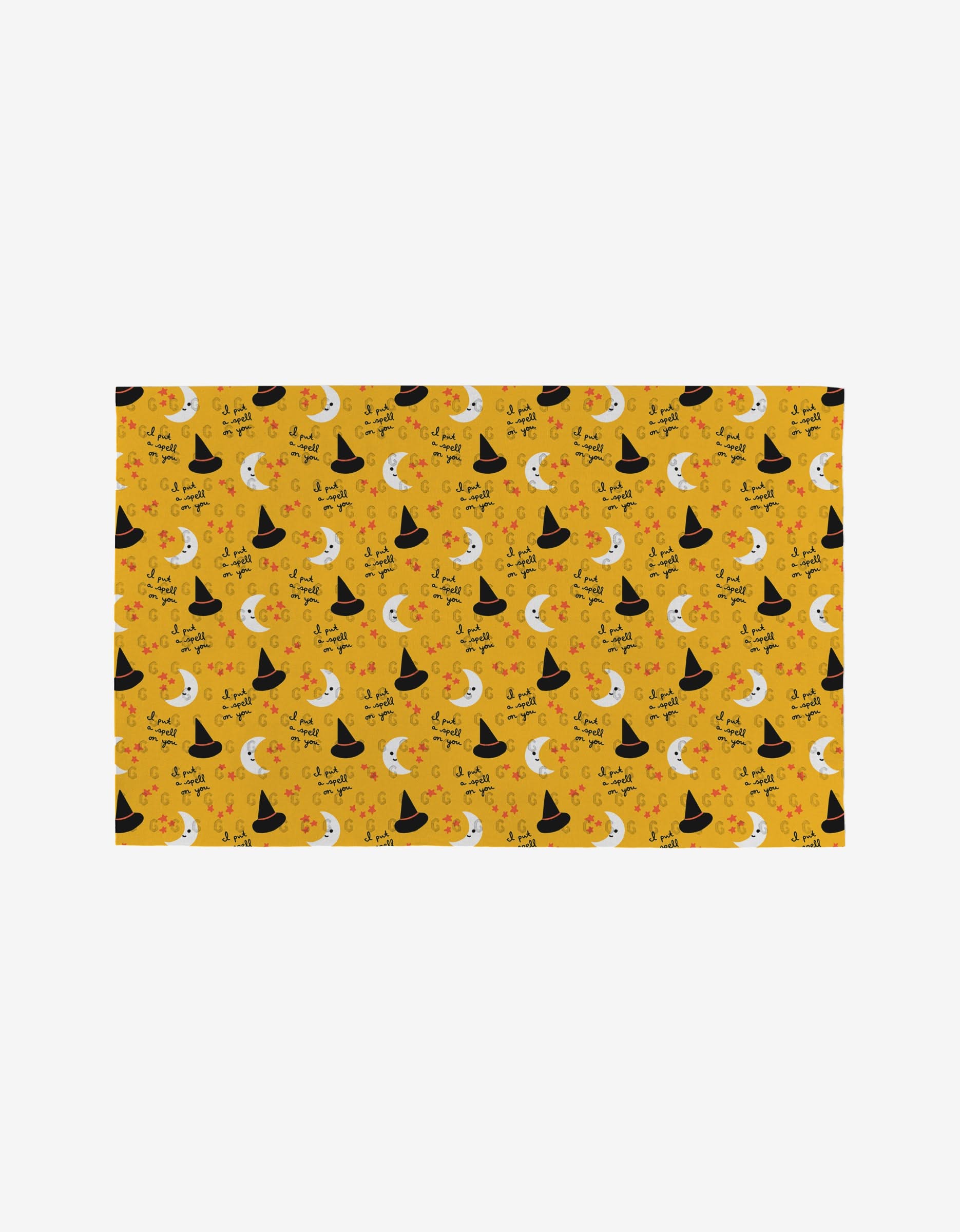 The Genna Blackburn Spooky Season mat is a yellow rectangle made from eco-friendly materials, featuring black witch hats, crescent moons, stars, jack-o’-lanterns, and “Trick or Treat”—perfect for reusable paper towels.