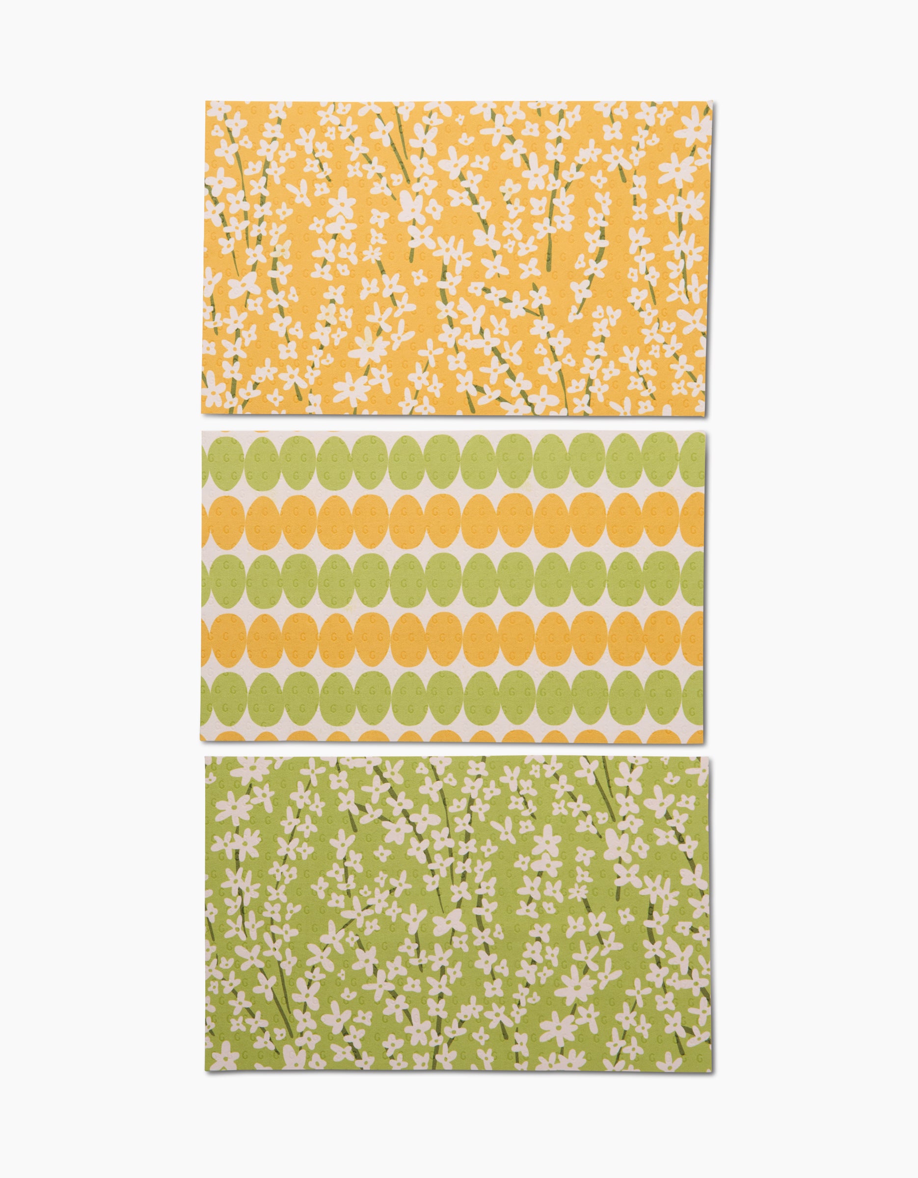 Kayla Ann’s Spring Bounty set features three rectangular sheets: one yellow with white florals, one with green and yellow circle rows, and one eco-inspired sheet—green with white floral patterns.