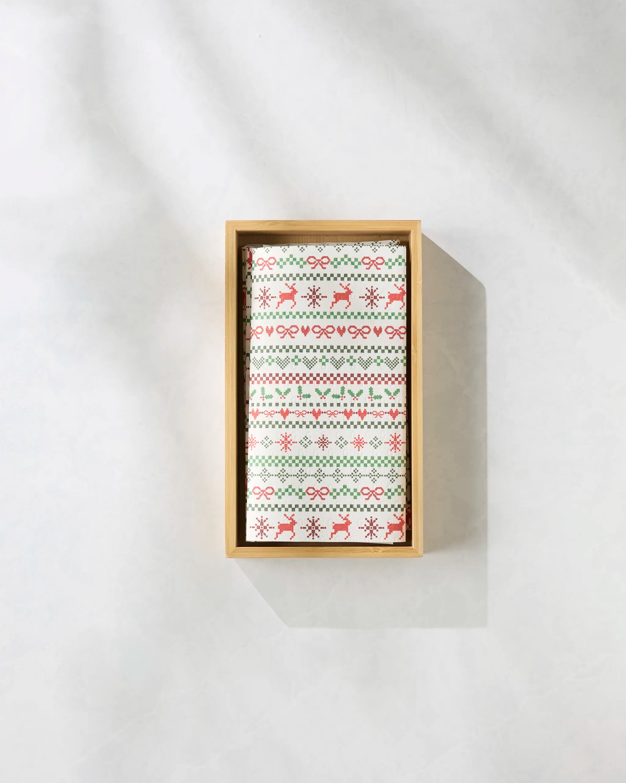A rectangular wooden box holds Geometry’s "Ugly Sweater Day" eco-friendly, reusable paper towels, featuring a festive red-and-green snowflake, diamond, and reindeer pattern, displayed on a light, shadowed surface.