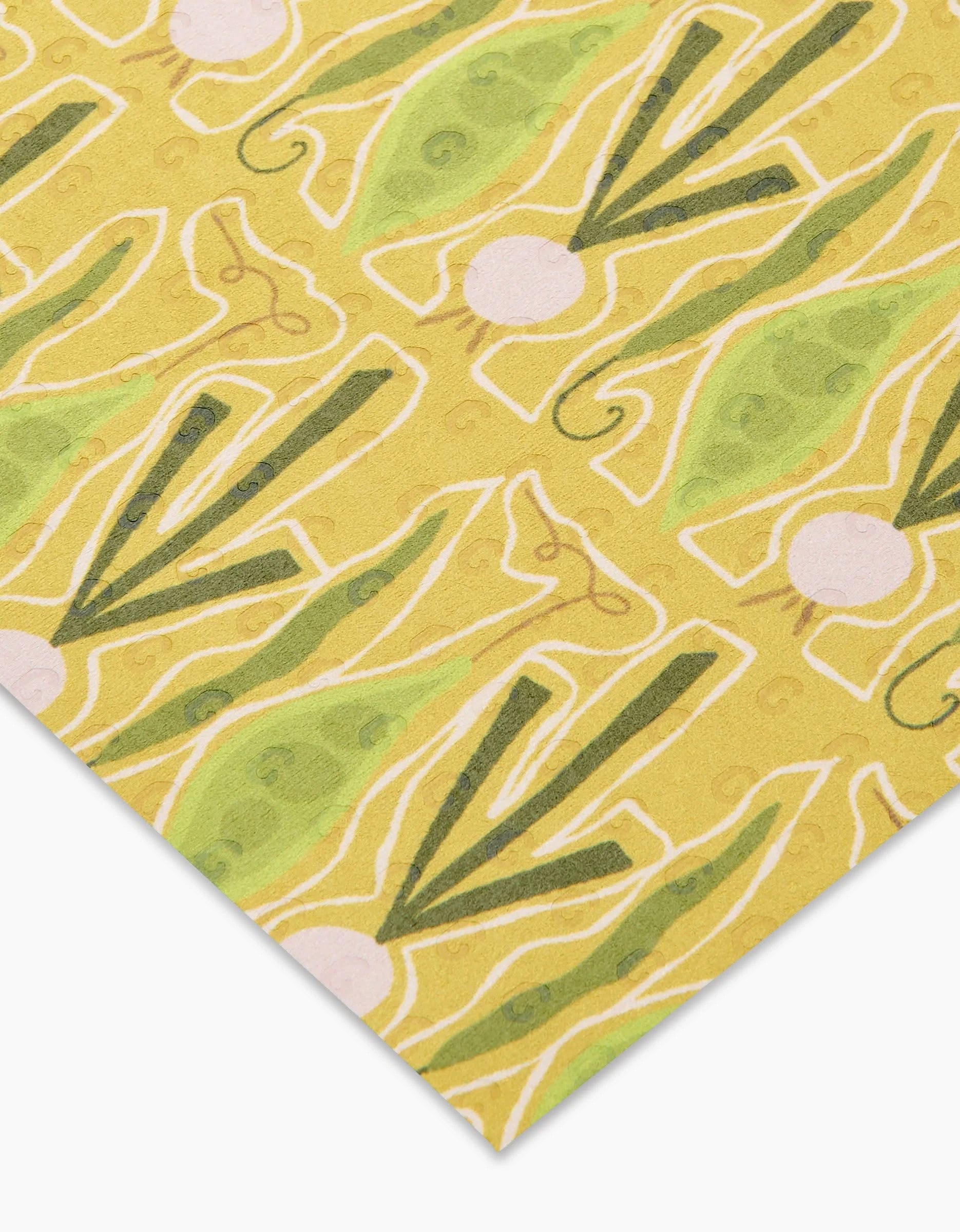 A close-up of Lizzie Clark’s Veg on Parade eco-friendly paper towels, featuring yellow material with green pea pod patterns, white circles, and abstract lines arranged at an angle.