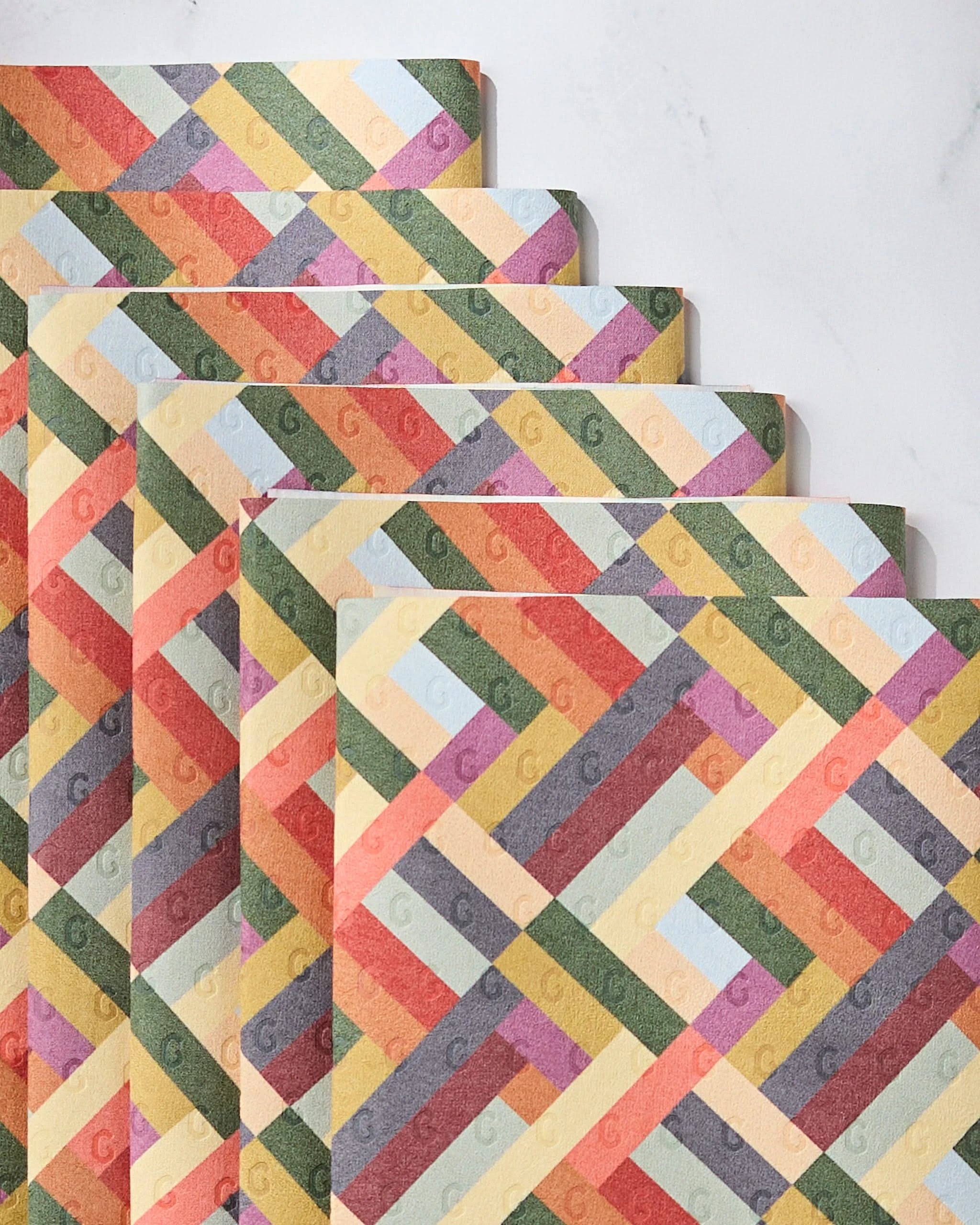 Vivid Cascade by Geometry features colorful, textured sheets with diagonal pastel stripes stacked in a geometric pattern—an eco-friendly kitchen towel that’s not paper.