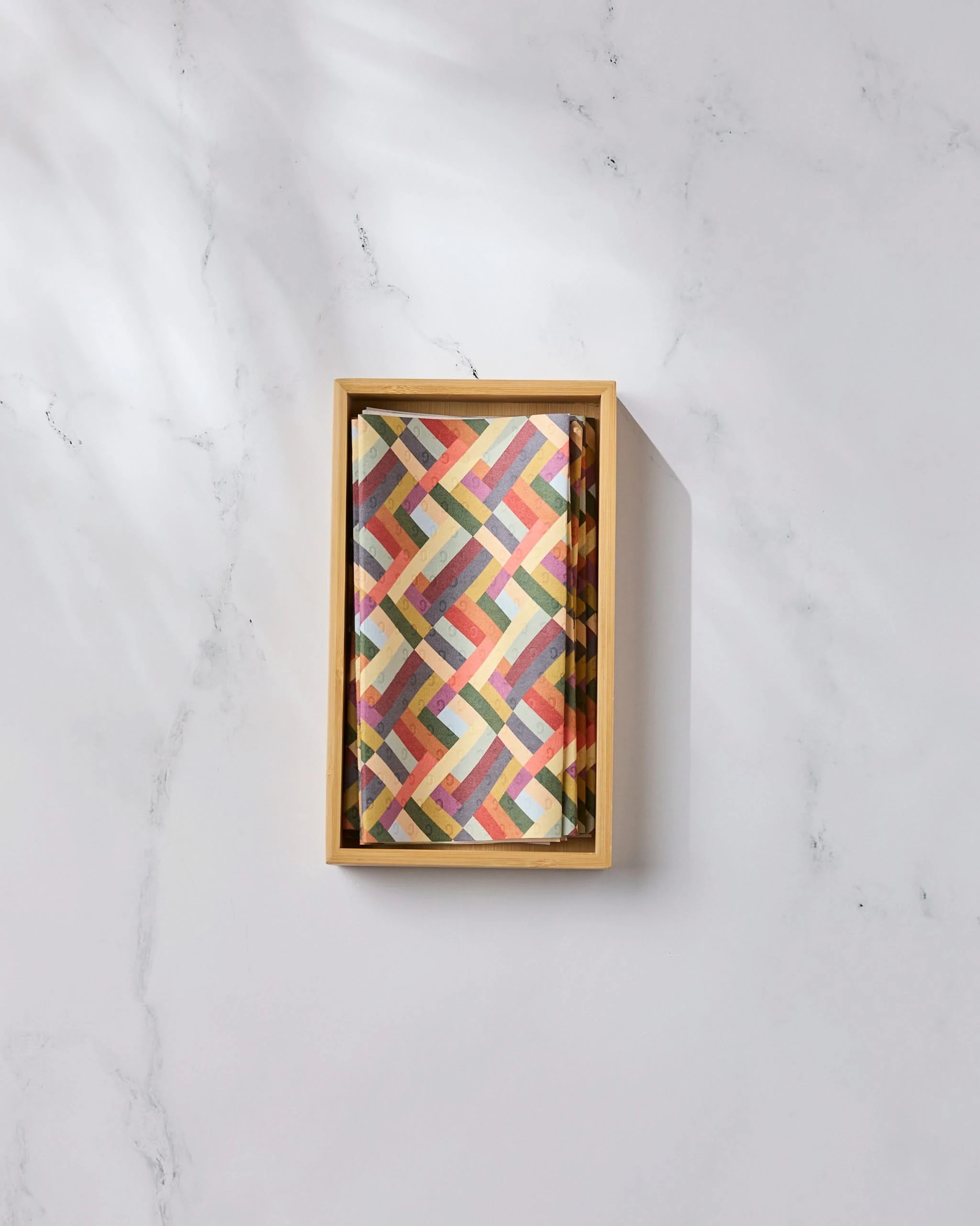 A rectangular box of Geometry’s Vivid Cascade—not paper towels—featuring a colorful, geometric crisscross pattern, sits on a white marble surface in soft natural light—an eco-friendly kitchen towel choice for your home.