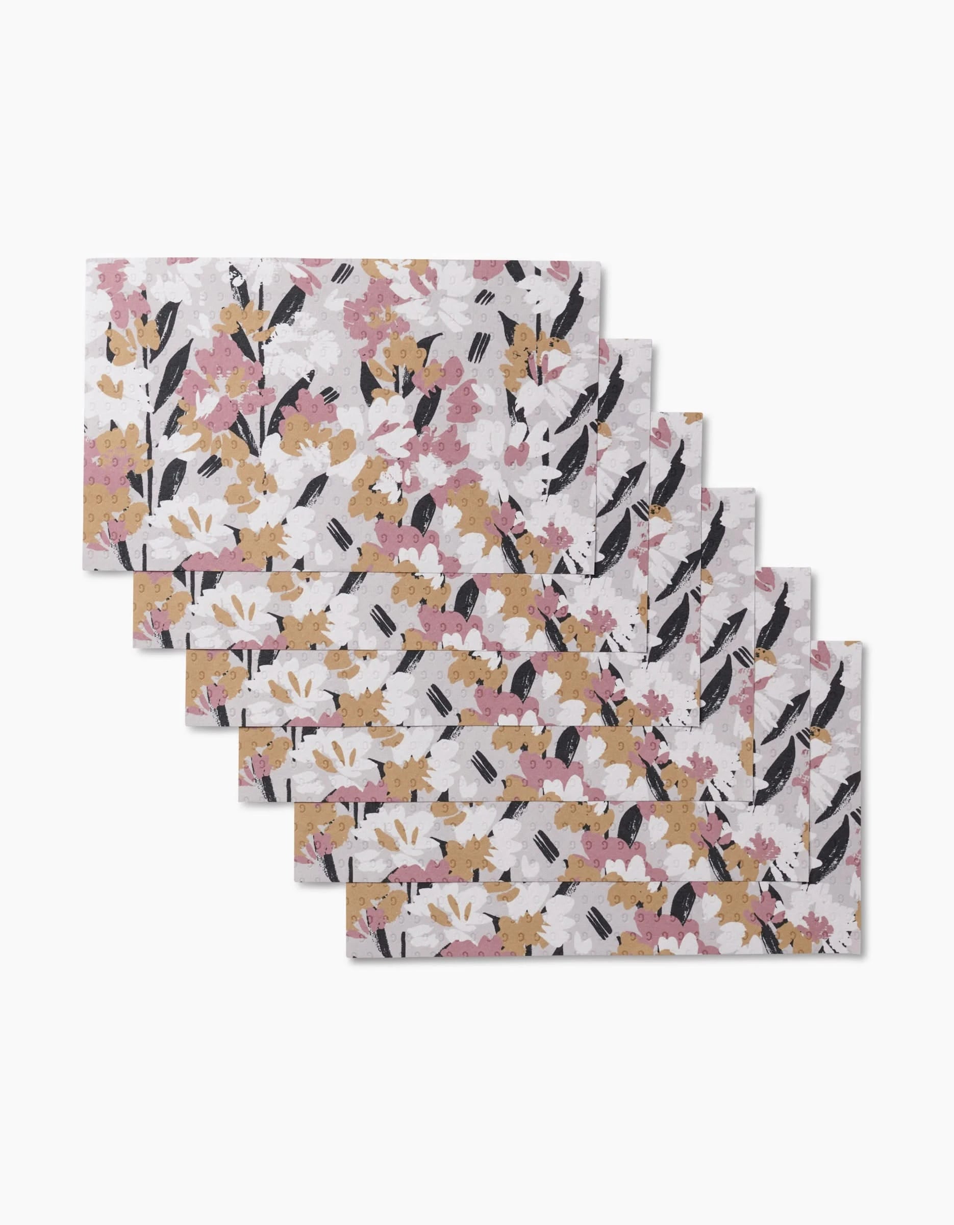 Six reusable Wilderness Floral placemats by Toboggan Avenue are stacked in a fanned display. Each shows yellow, pink, and white flowers with black leaves on a light background—a sustainable alternative to paper towels.