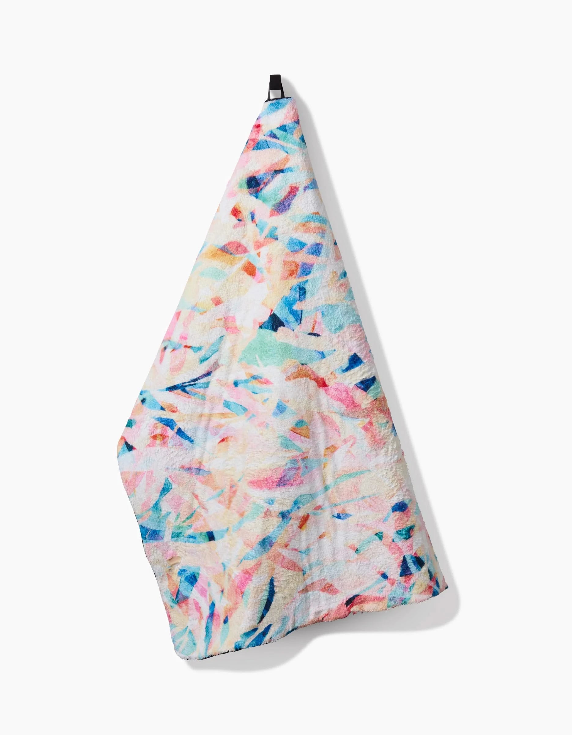The Rachel Parker Abstract Jungle towel features a vibrant pastel abstract pattern and ultra-absorbent fabric, shown hanging from a black loop against a white background.
