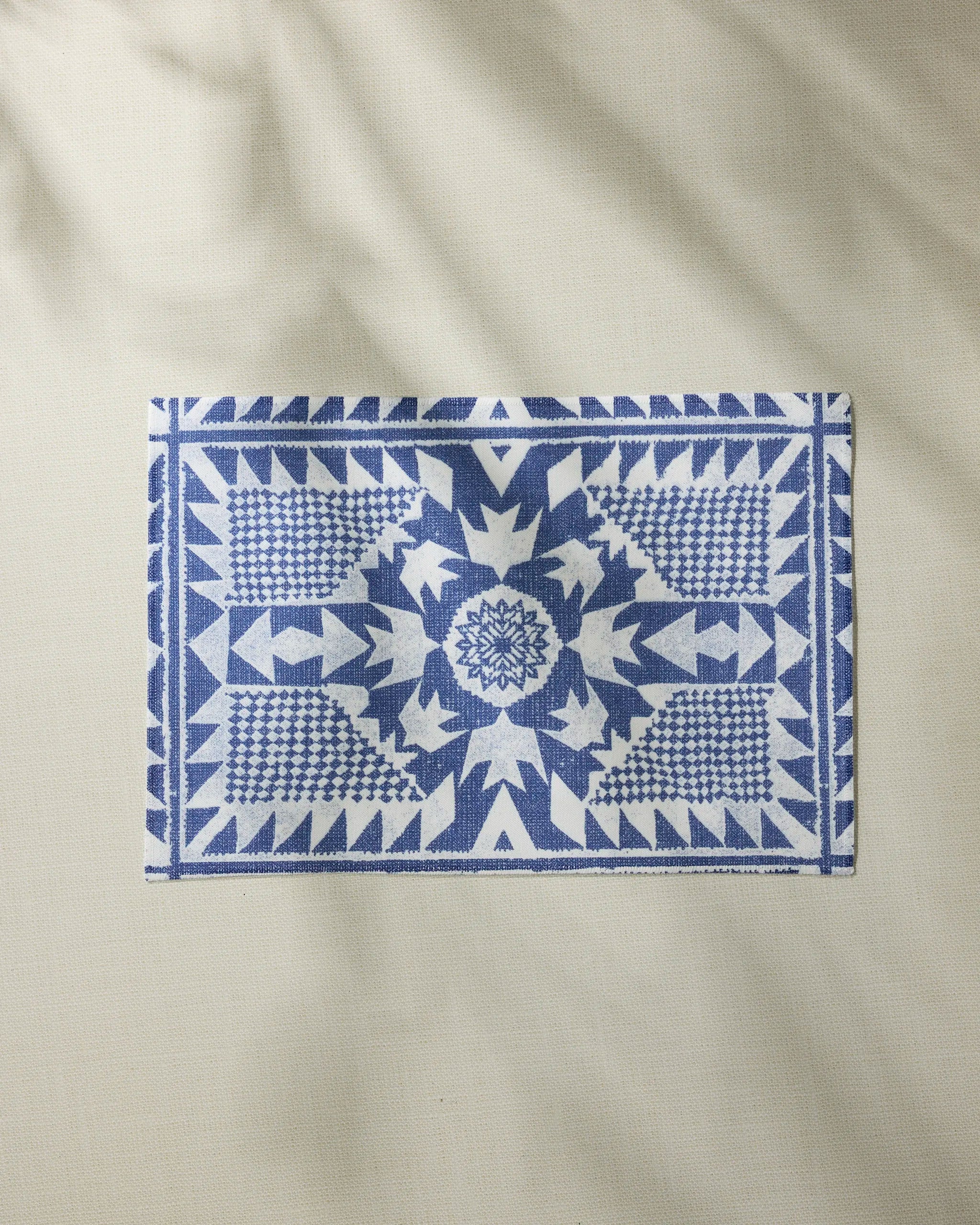 The Geometry Bluebird Placemat by Geometry, featuring geometric blue and white designs, is displayed on a light beige background. This machine-washable placemat combines style and practicality for your dining area.