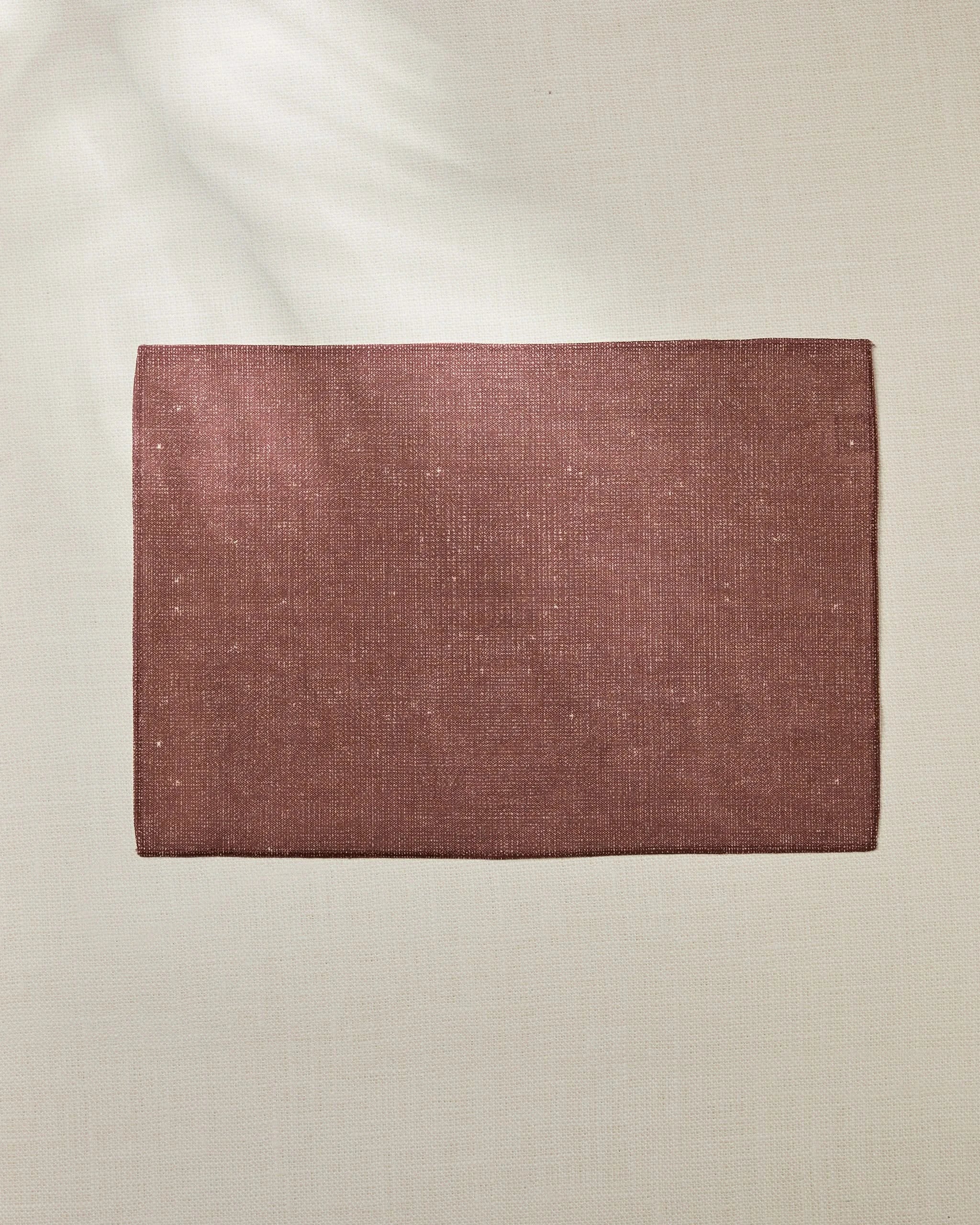 The Geometry Russet placemat, a rectangular textured piece made from eco-friendly materials in dusty rose, rests on a light beige surface with soft natural light creating faint shadows in the upper left corner.