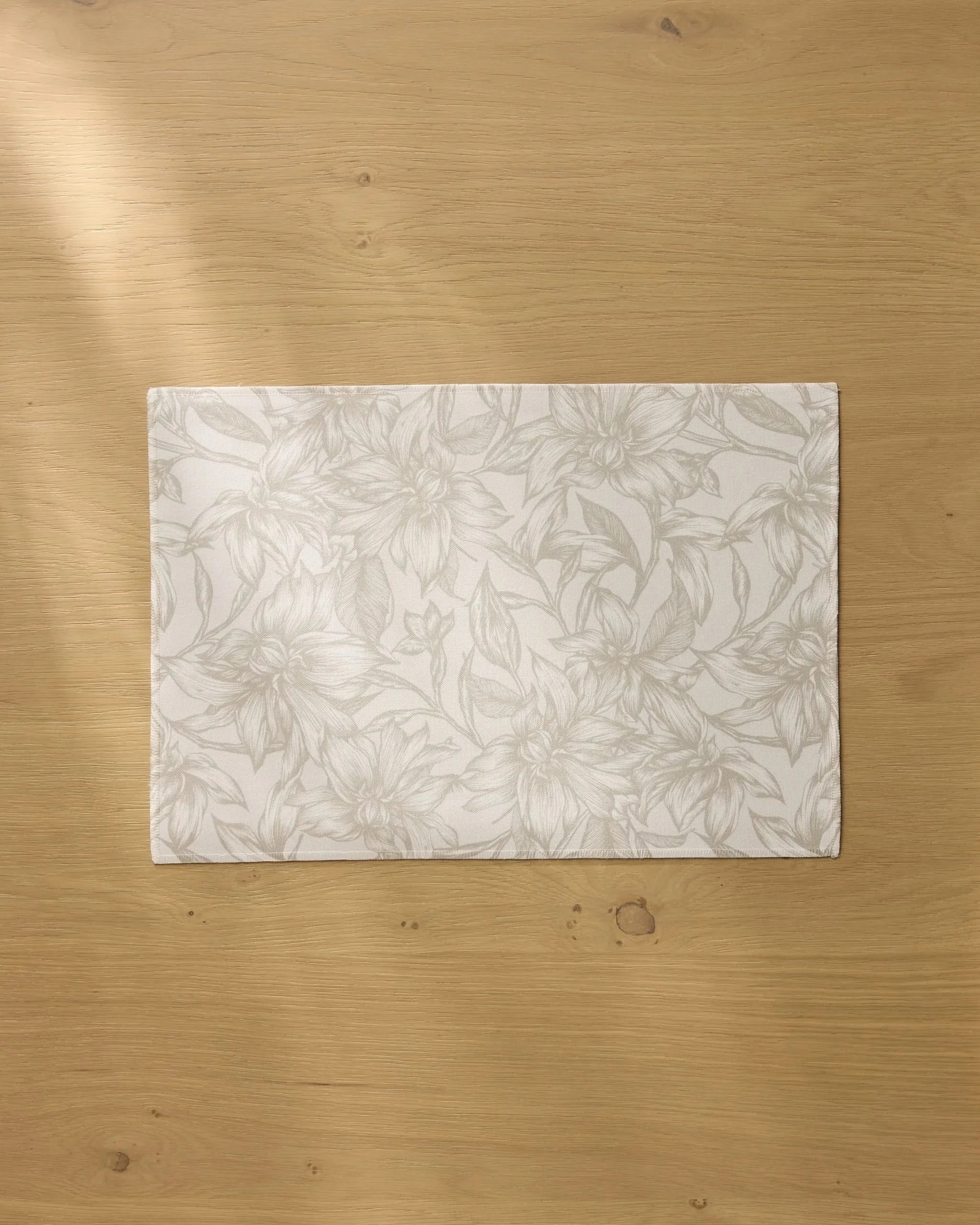 The Geometry Alba rectangular white recycled placemat, featuring a subtle floral pattern, rests on a light wooden table bathed in soft natural light.