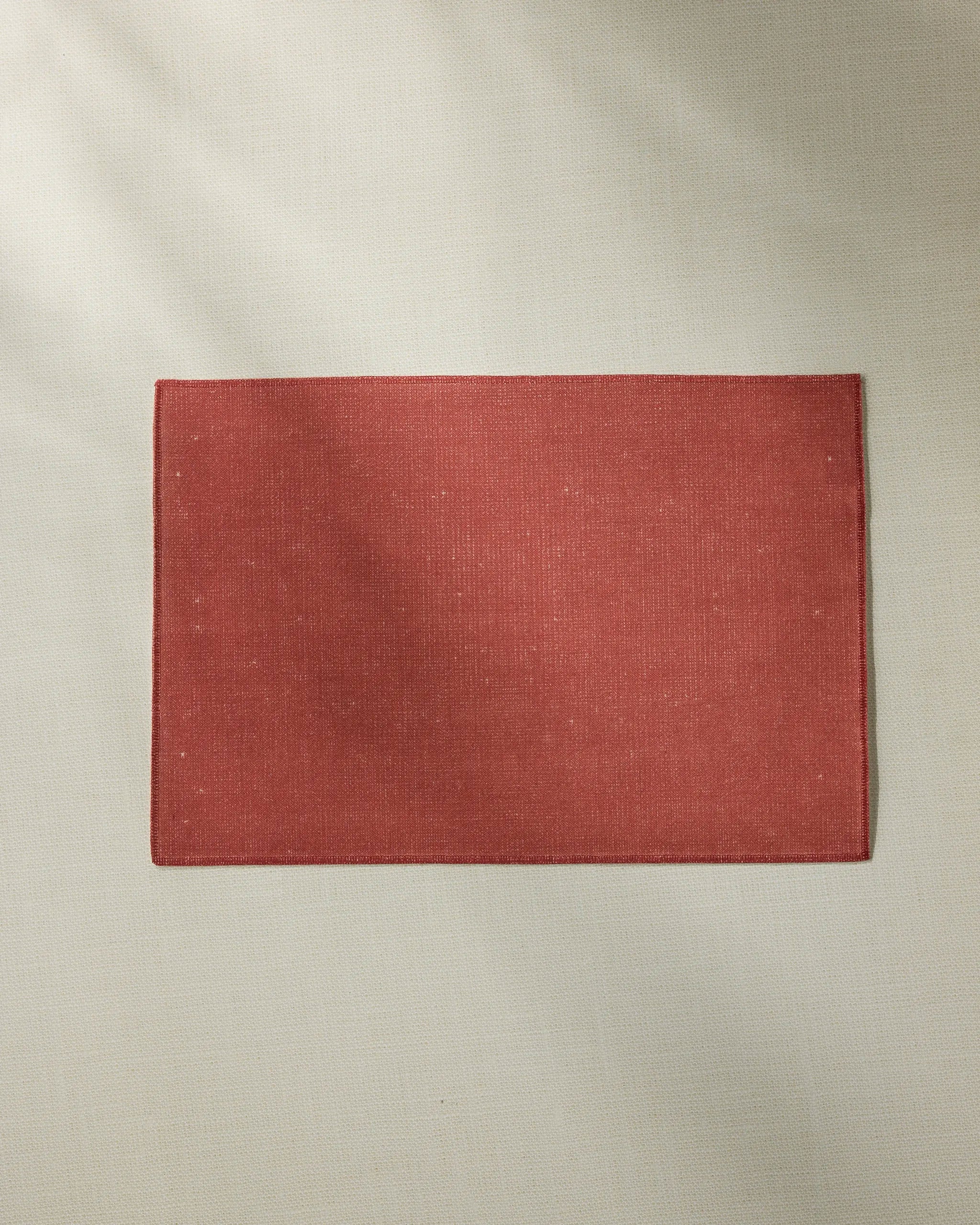 The Geometry Crimson placemat, rectangular and red, is centered on a light beige fabric surface—made from recycled materials and fully machine washable for easy care.