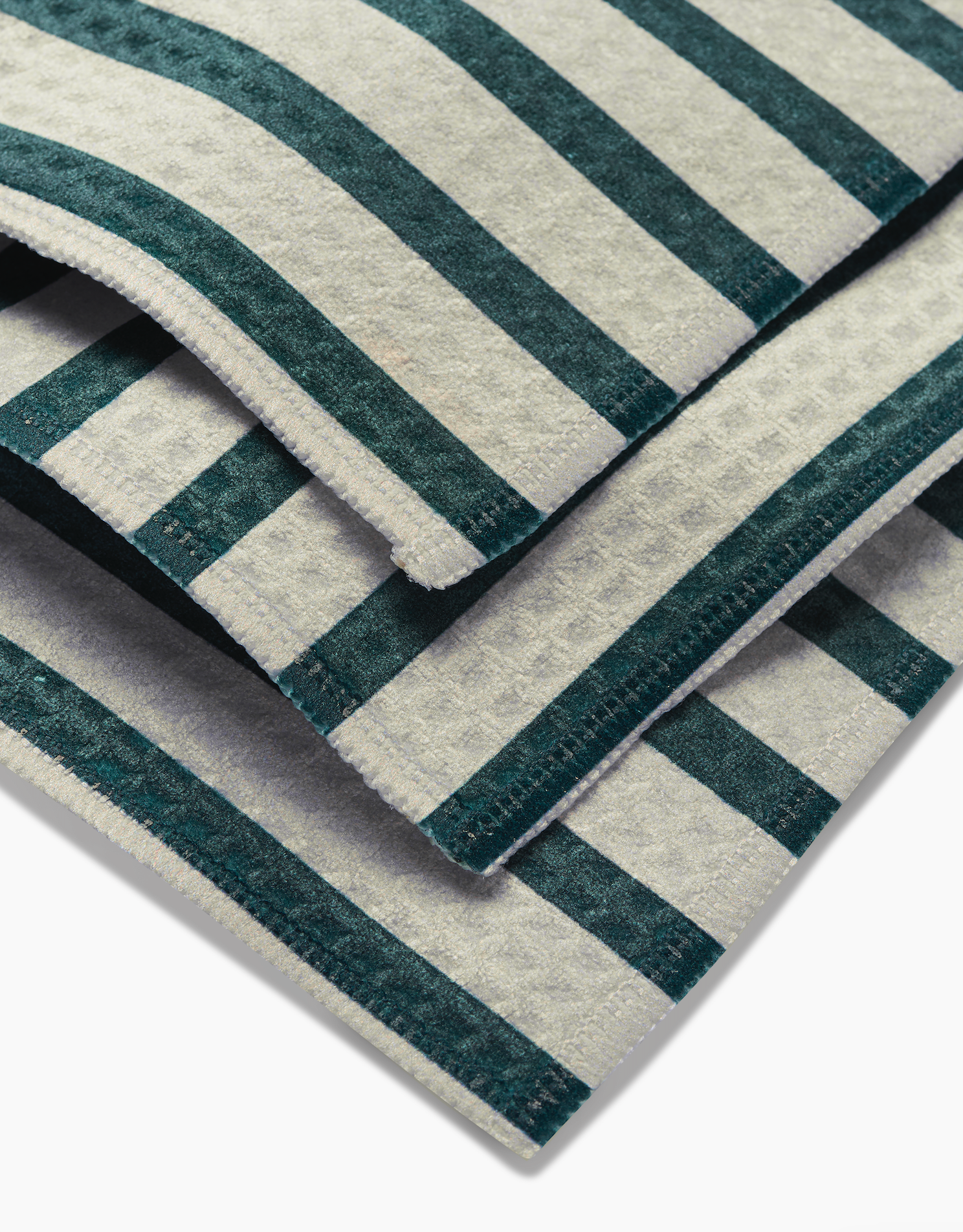 A close-up of GEOMETRY Deep Green Stripes washcloths shows their green and white striped pattern, detailed fabric texture, and Geoweave-crafted edges, all set against a white background.