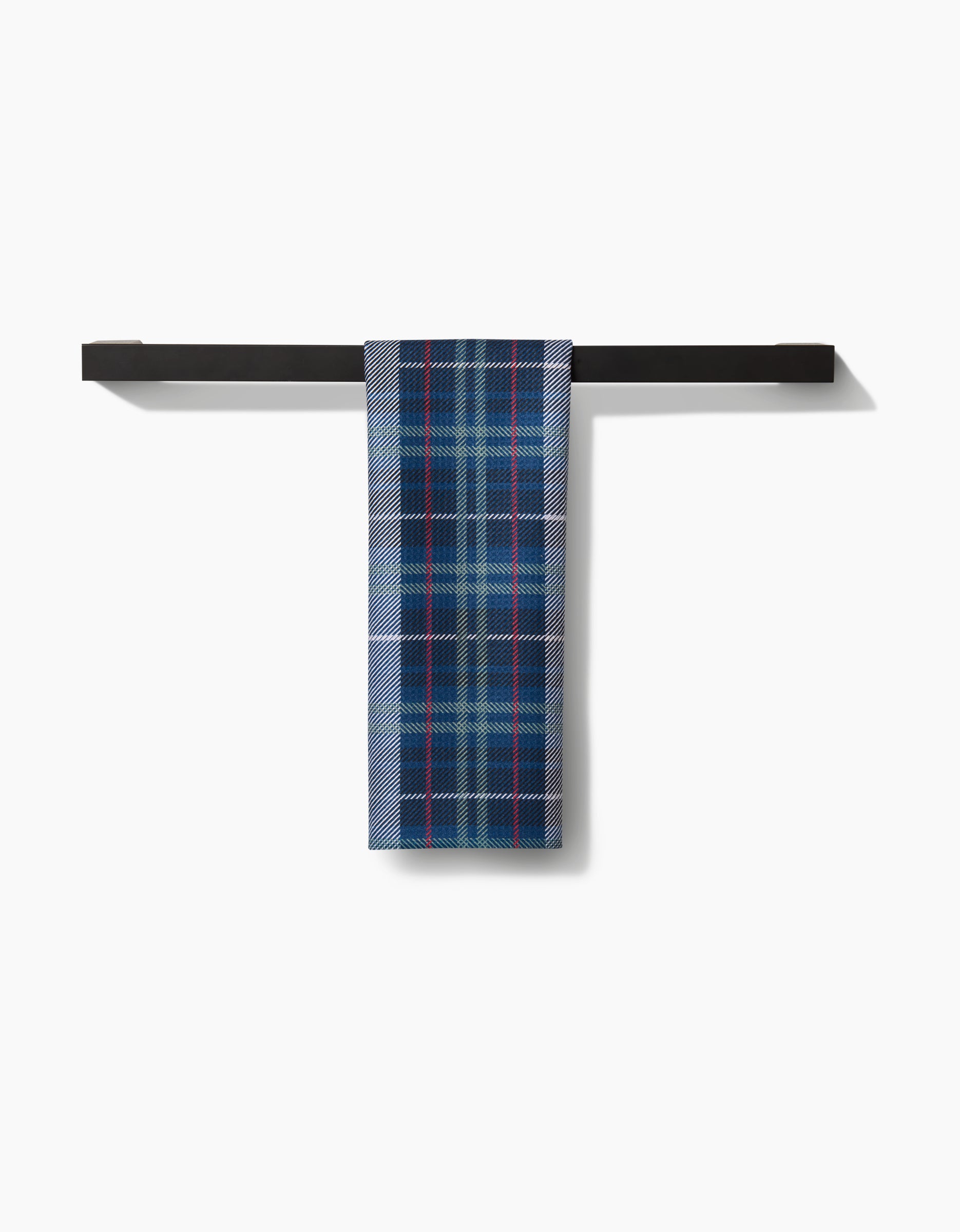 The Scotty Tea Towel by Becki Owens, featuring a blue, white, and red plaid pattern, hangs over a sleek black horizontal bar. Made with premium Geoweave™ fabric for style and durability against a white background.
