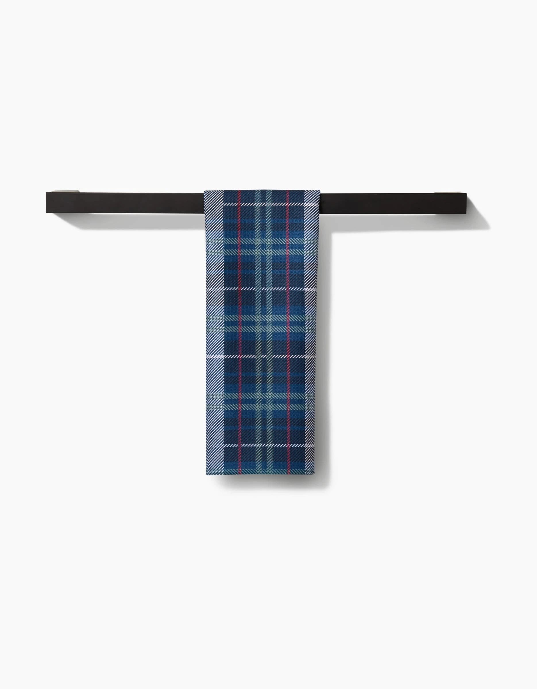 The Scotty Tea Towel by Becki Owens, featuring a blue, white, and red plaid pattern, hangs over a sleek black horizontal bar. Made with premium Geoweave™ fabric for style and durability against a white background.