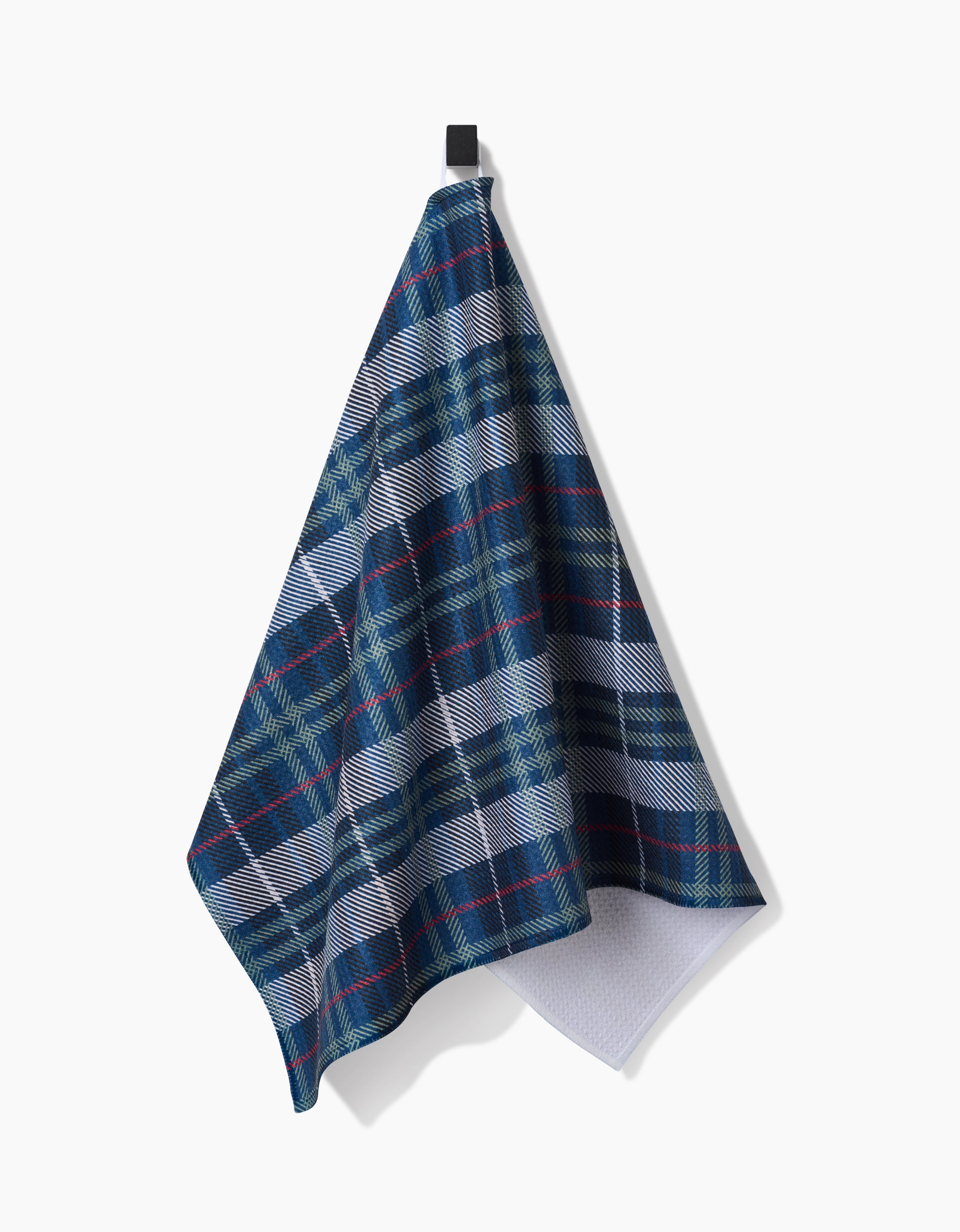 The Scotty tea towel by Becki Owens, featuring blue, green, and white plaid with red accents in Geoweave™ fabric, hangs from a black hook against a white background.
