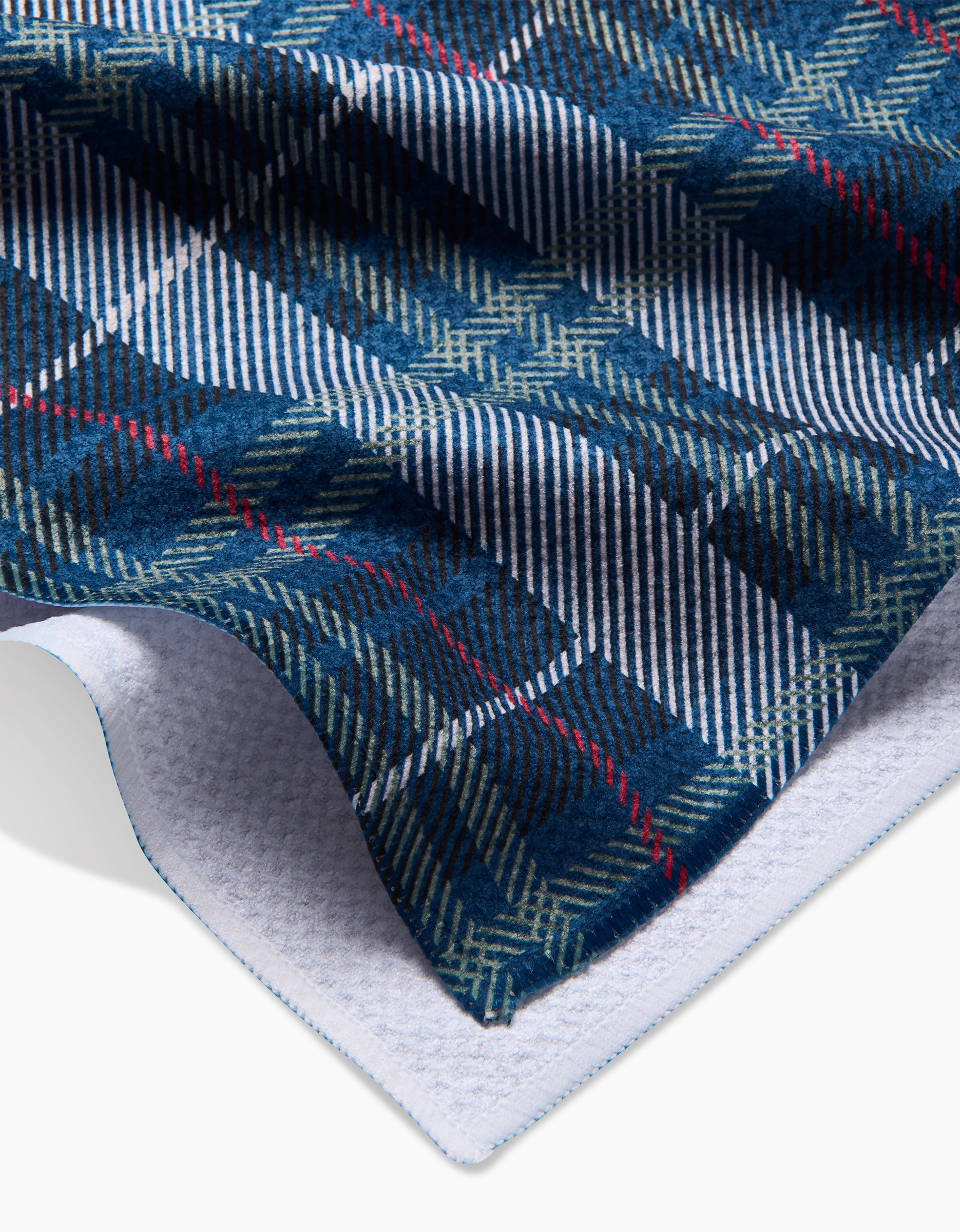 A close-up of the Becki Owens Scotty tea towel, featuring blue, green, and white plaid with thin red lines, folded to display its white textured Geoweave™ fabric underside.