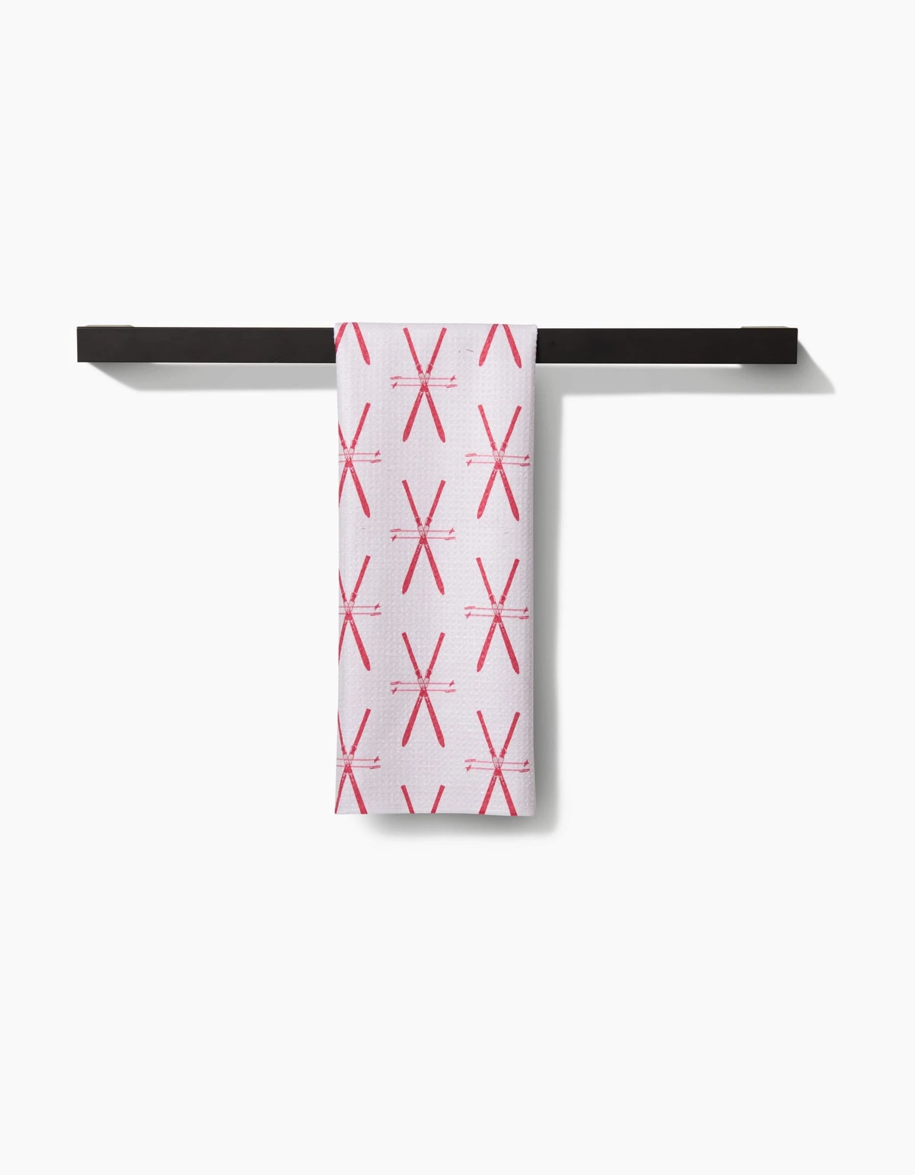 A Becki Owens Vintage Ski Tea Towel, featuring a charming vintage ski design, hangs neatly on a black towel bar against a white background, crafted from eco-friendly Geoweave fabric for style and sustainability.