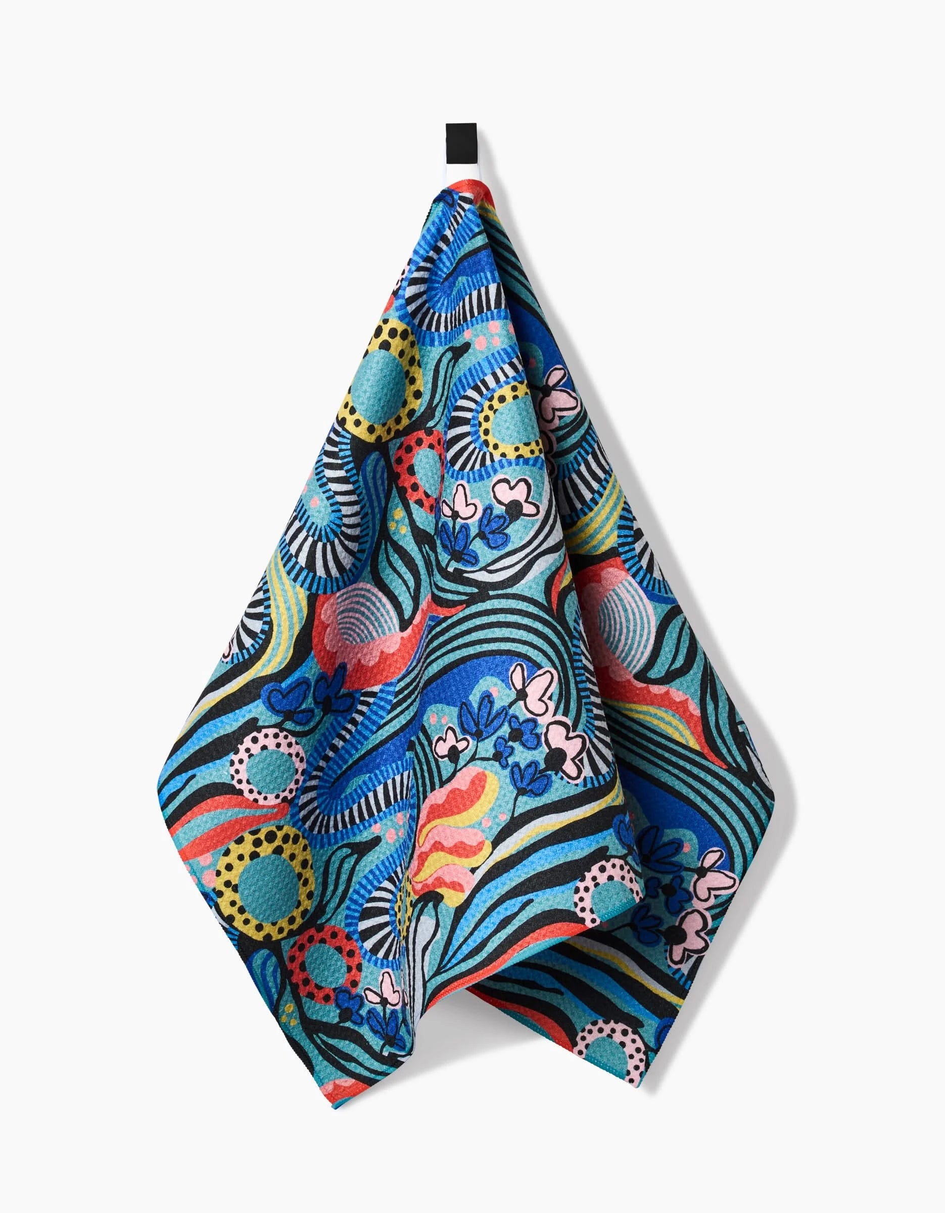 The “Abstract Dreams” tea towel by Masha Volnova features a vibrant floral and wave pattern in blue, green, yellow, pink, red, and white. Made from Geoweave fabric, it hangs from a black hook against a white background.