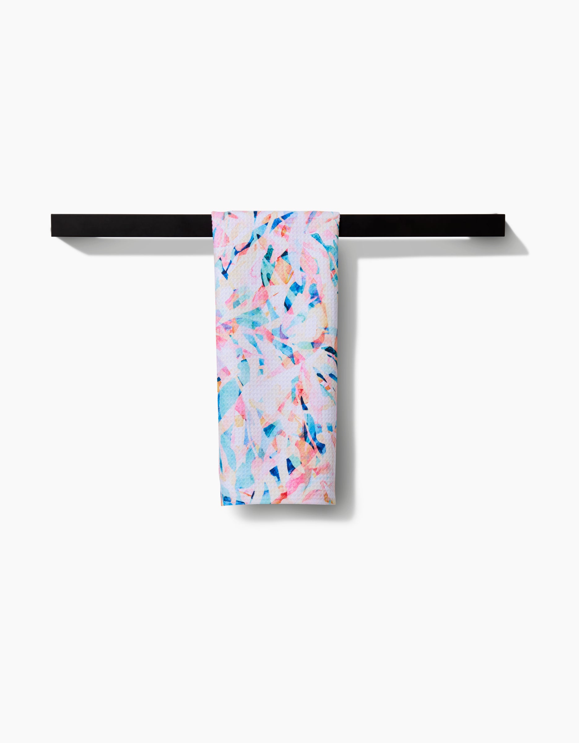 The Rachel Parker Abstract Jungle tea towel, featuring a colorful pastel pink, blue, and white abstract pattern, hangs neatly on a sleek black towel bar against a white background.