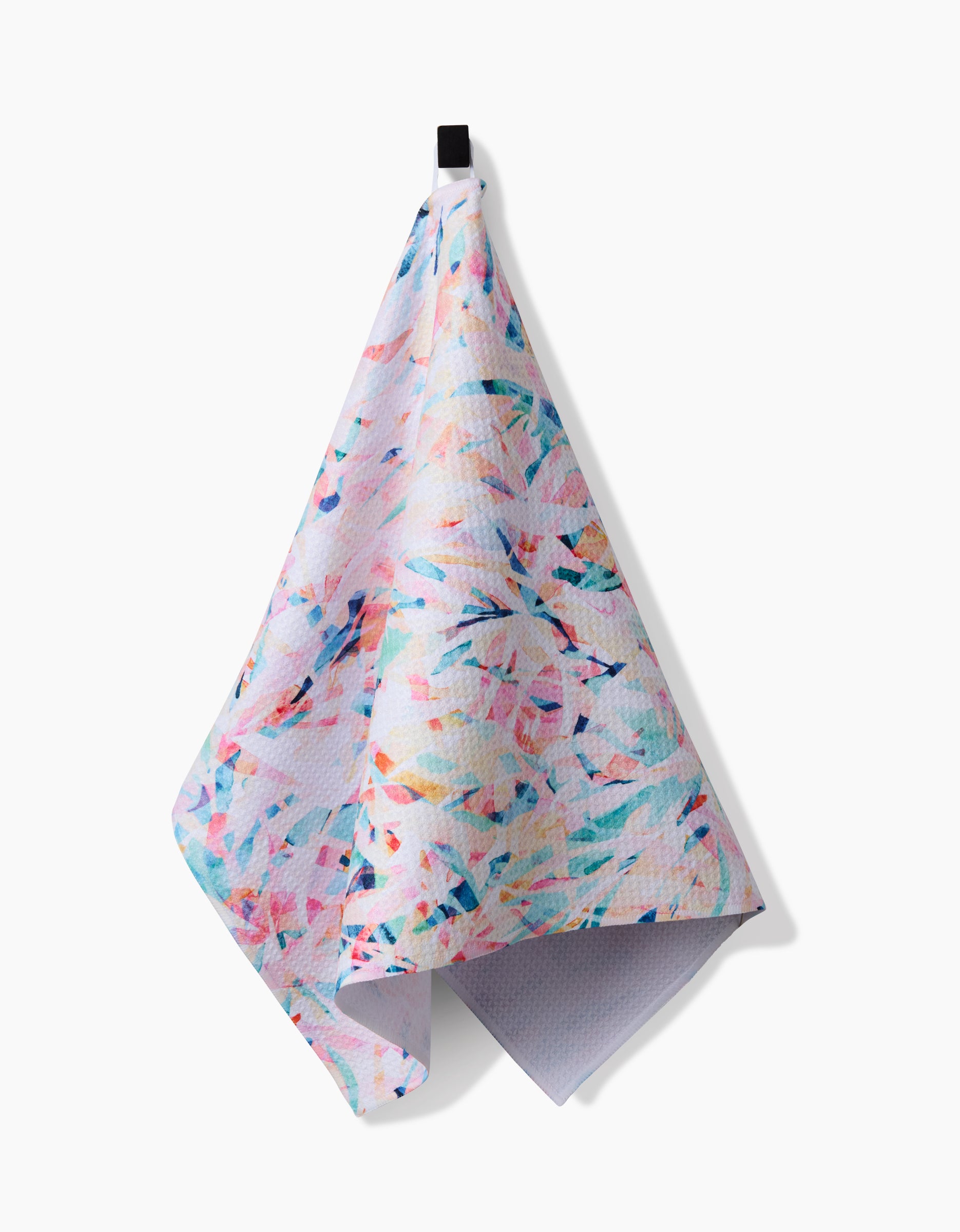 The Abstract Jungle Tea Towel by Rachel Parker, crafted from Geoweave fabric, hangs from a black hook. Its pastel painterly design features splashes of pink, blue, yellow, and purple against a white background.
